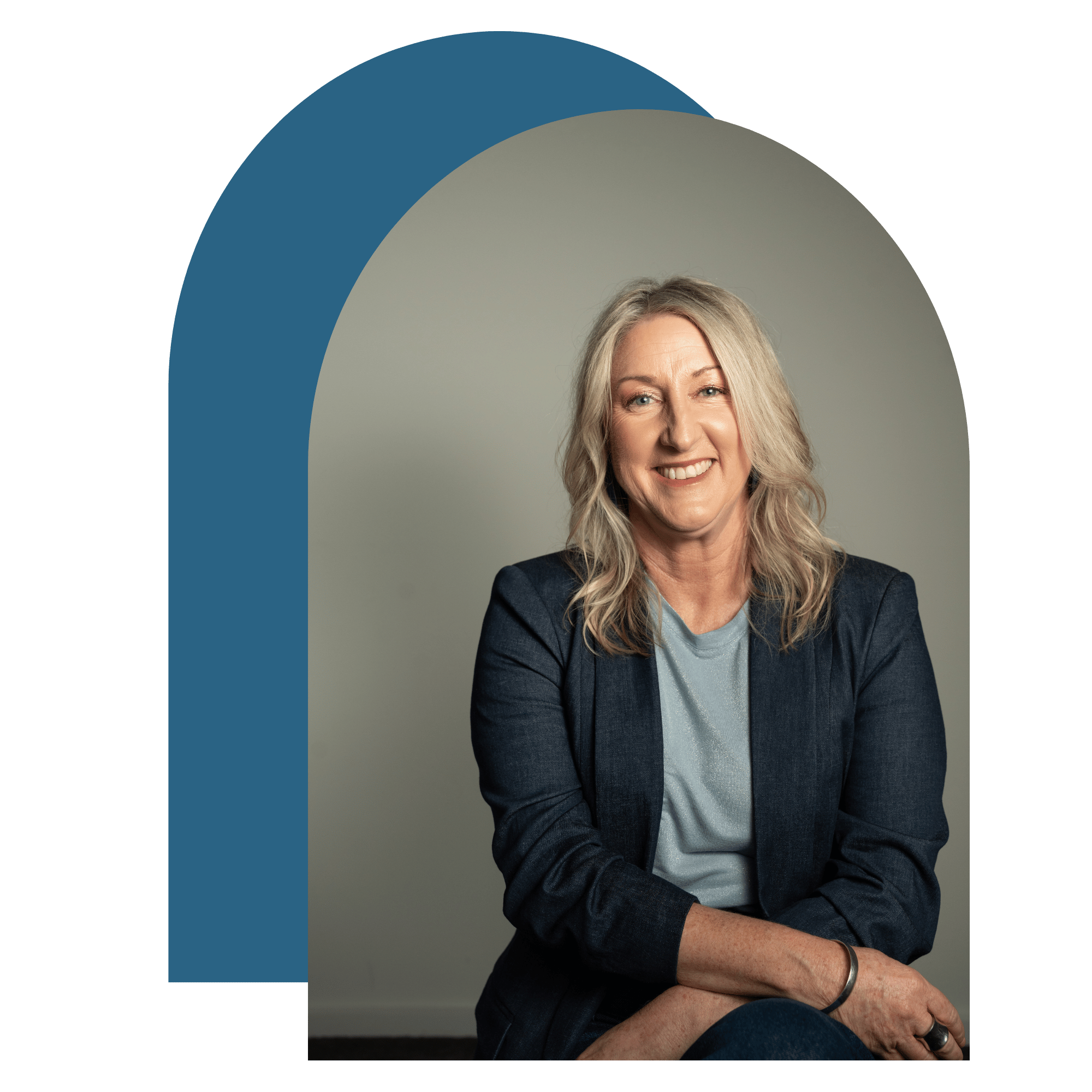 Headshot of a middle-aged woman with long blonde hair, smiling, wearing a dark blazer and light blue top, seated against a neutral background with a graphic element.