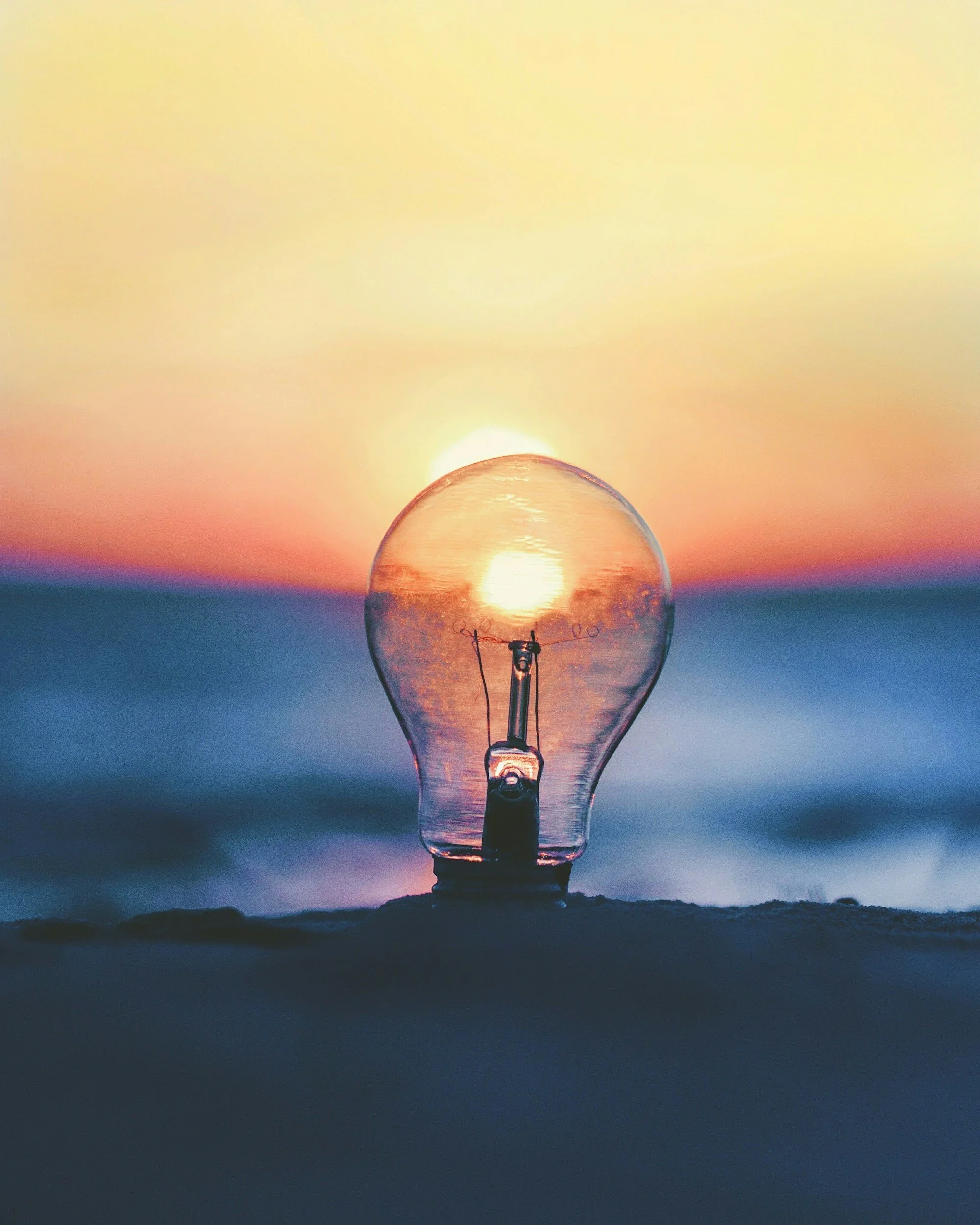 Warm glowing lightbulb against a dark background representing insight and clarity through strengths-based coaching