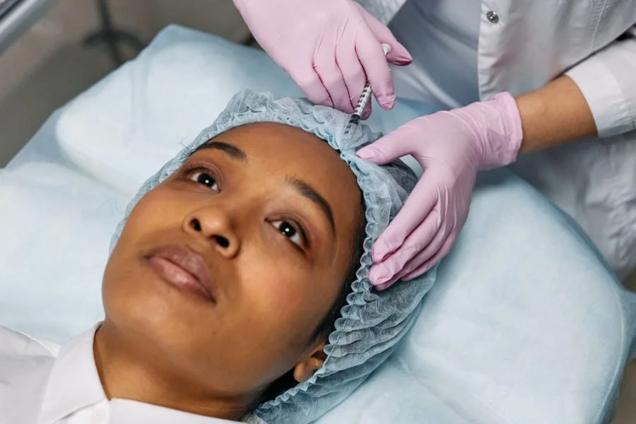 Medical professional administering a facial filler injection to a woman's forehead in a clinical setting.