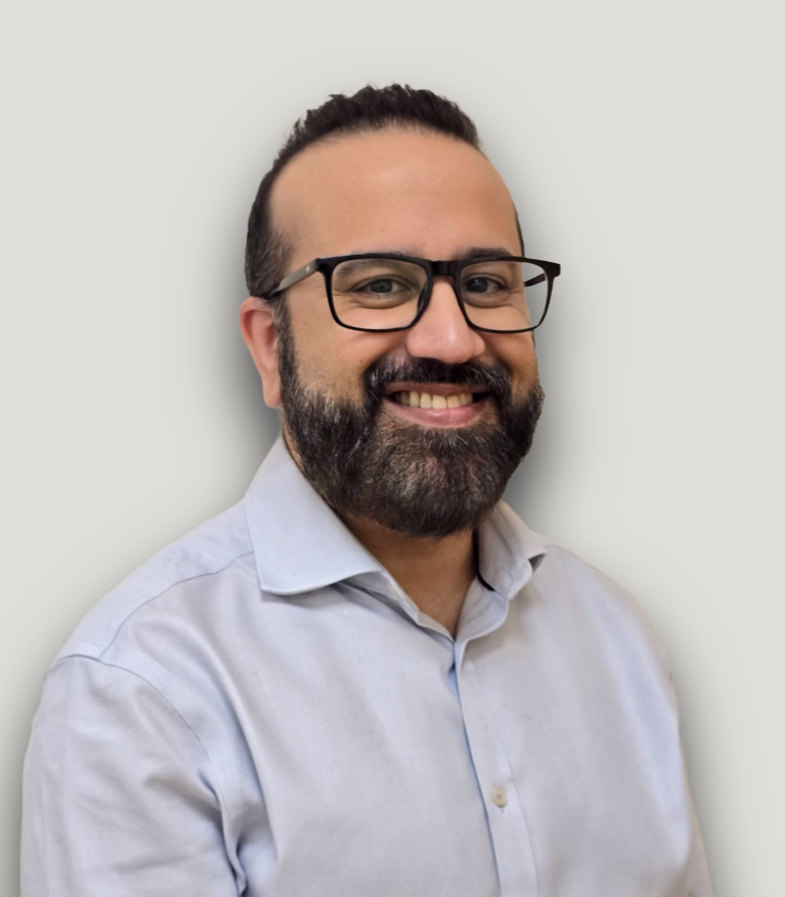 Doctor Roy Parijat. A man with dark hair, glasses, and a beard, smiling in front of a plain, light-colored wall, wearing a white button-up shirt.