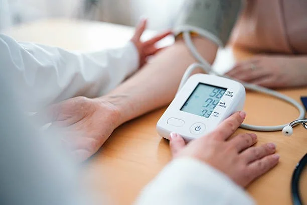 A clinician measuring blood pressure with a digital monitor while resting their arm on a table.