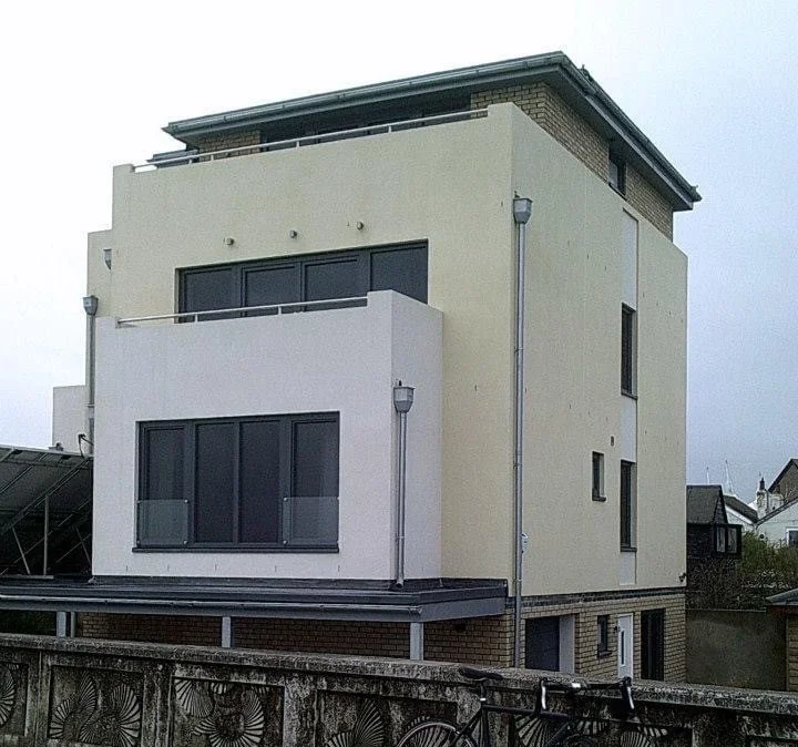 Multi-story modern residential building with large windows and a flat roof, located behind a concrete wall with a decorative pattern.