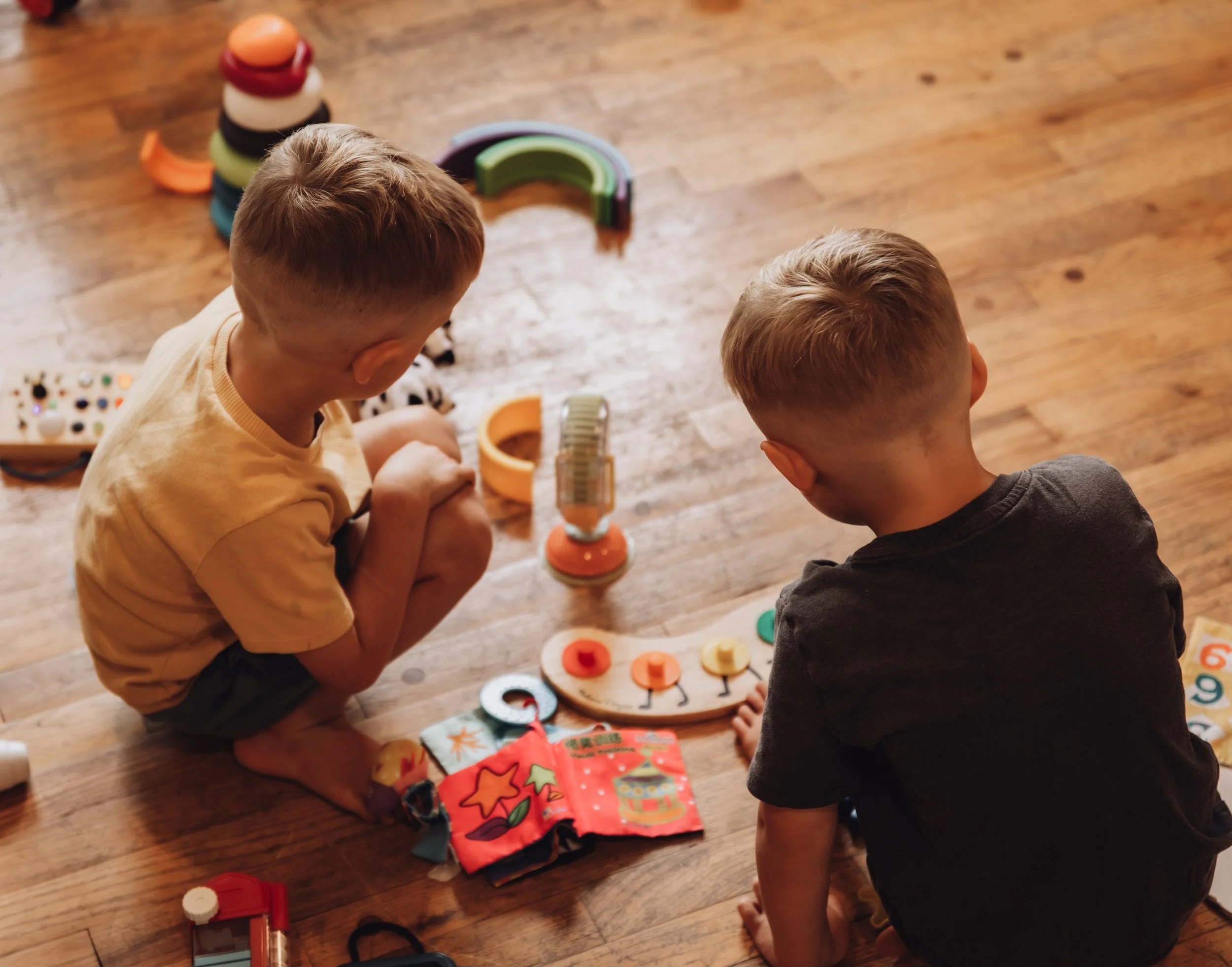 Two children playing with educational toys and colorful fabric items on a wooden floor.