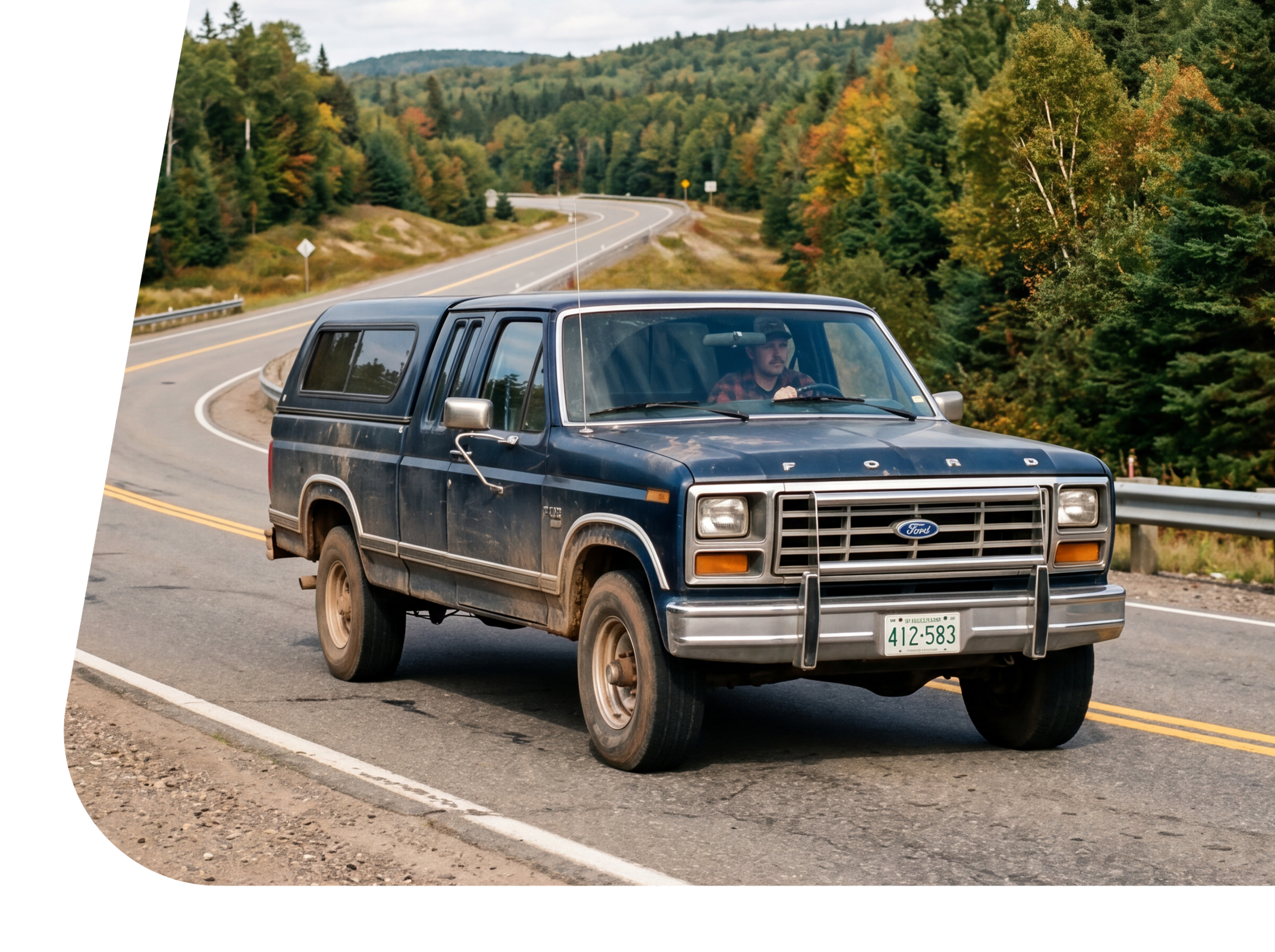 A black Ford pickup truck with an older model design driving on a winding mountain road surrounded by green trees and hills.