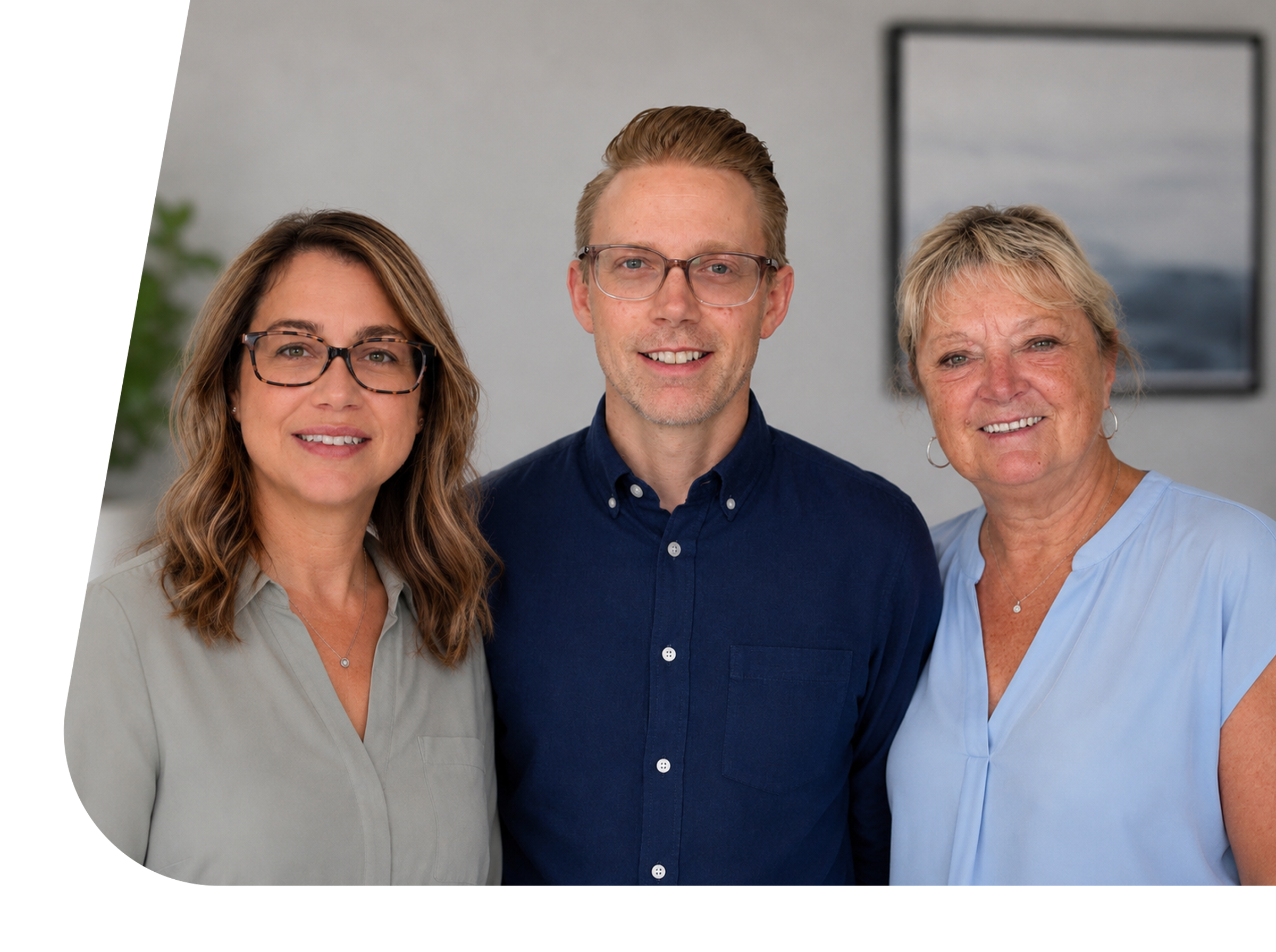 Three women and one man standing together indoors, smiling, with a framed picture and a plant visible in the background.