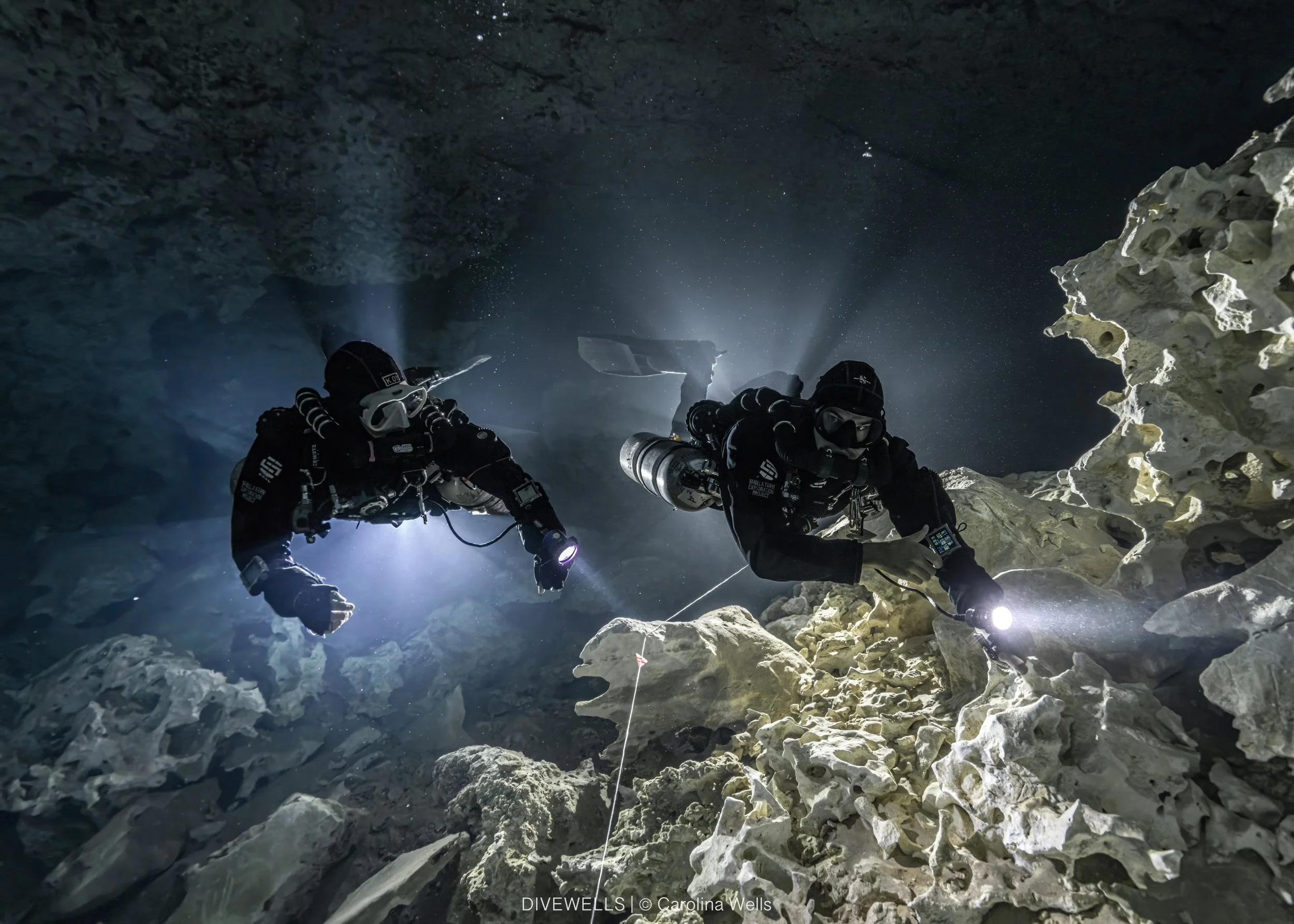 Two cave divers in a bright white cave with halo backlight