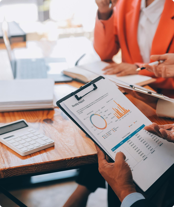 Business person holding a financial report with charts and graphs at a desk with a calculator and other documents.