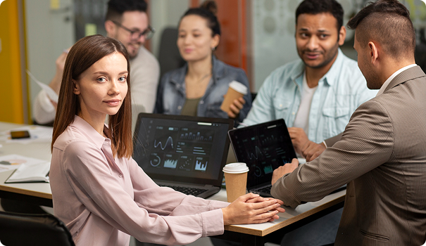 A group of five diverse professionals in a meeting room, with laptops and a tablet, engaged in discussion.