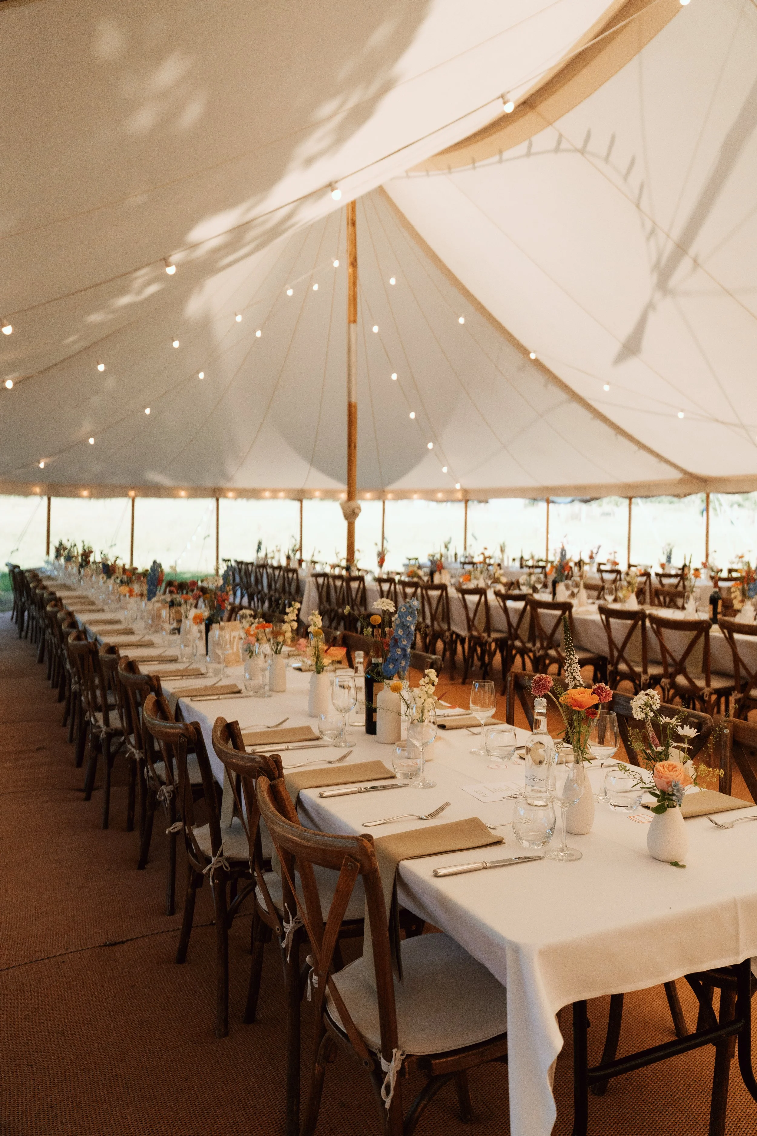 Elegant wedding breakfast table decorated with flowers beneath a sailcloth marquee in Sevenoaks, Kent.
