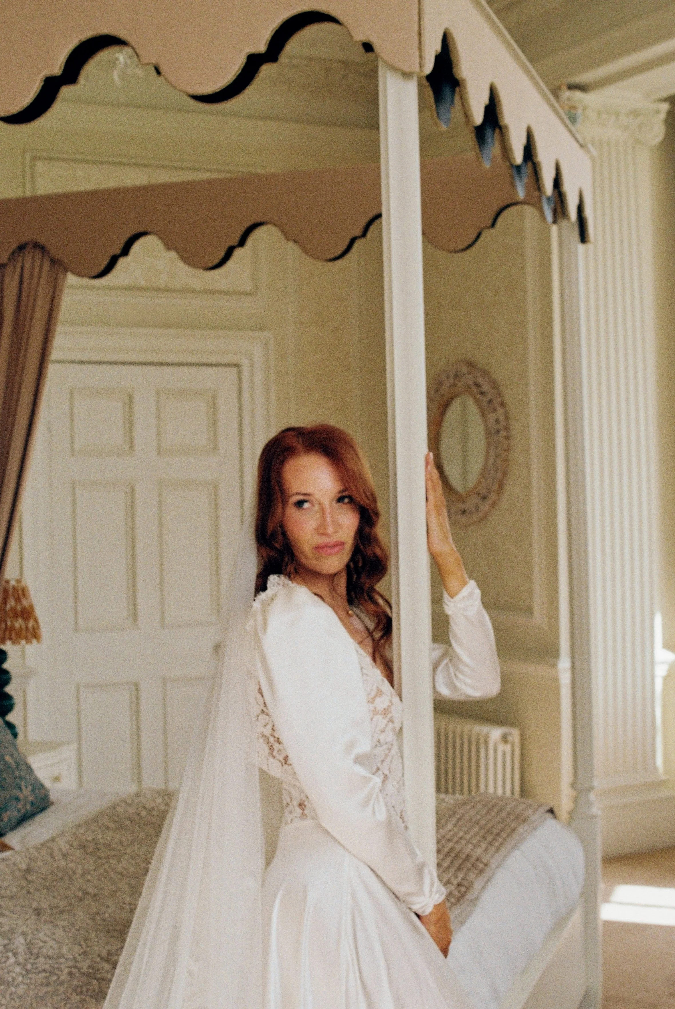 A bride with long red hair wearing a white dress in the bridal suite at Hedsor House.