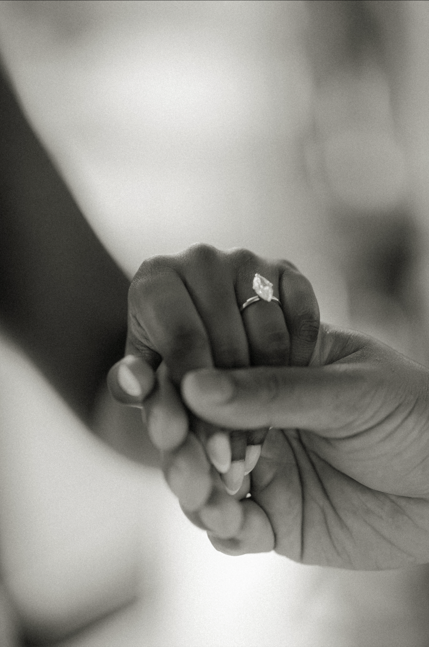 Close-up of two hands holding a person's hand with an engagement ring on the finger.