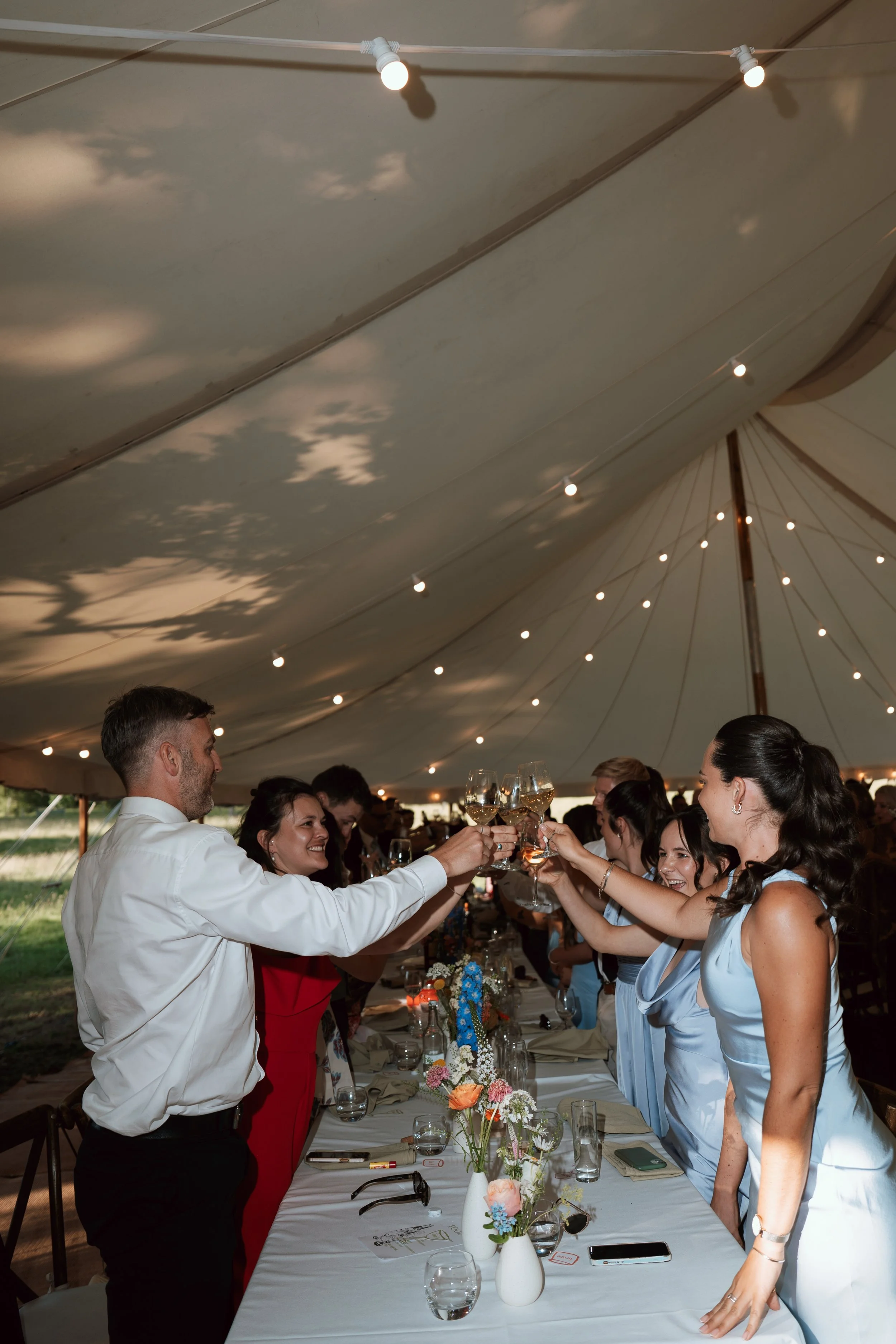 Wedding guests raising their glasses during a toast beneath a sailcloth marquee in Kent