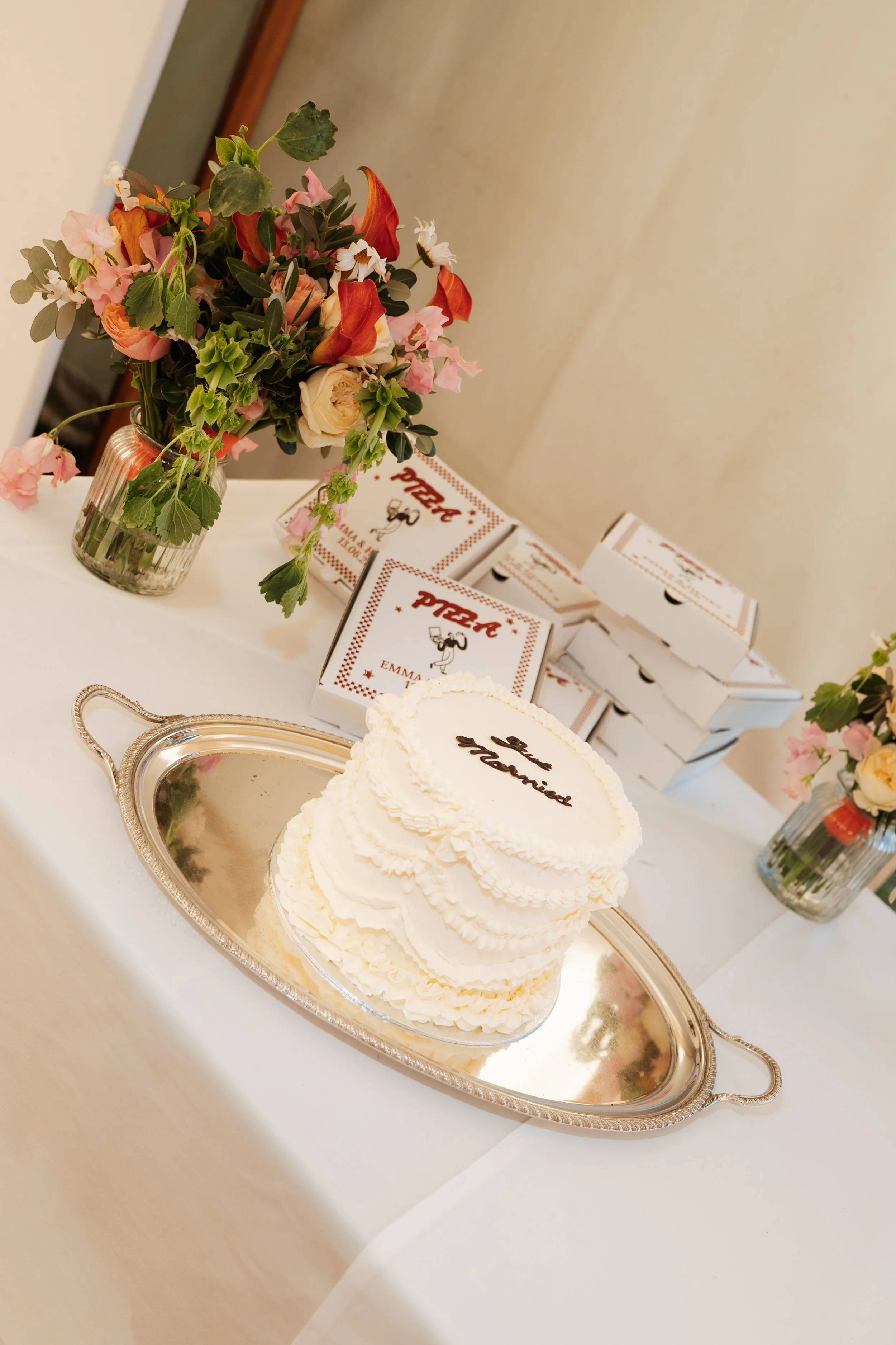 White wedding cake surrounded by colourful floral arrangements at a Sevenoaks wedding