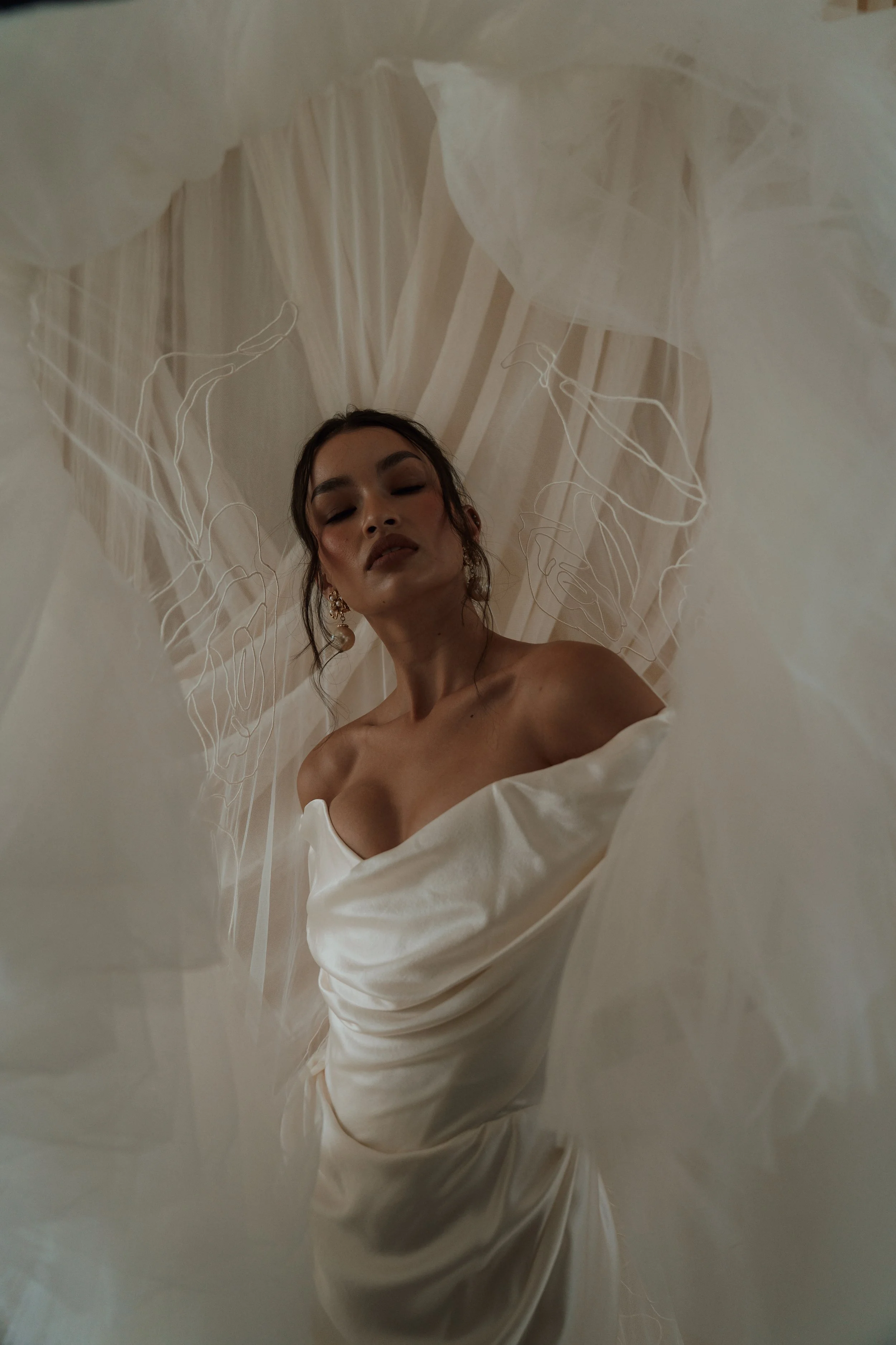 An intimate, artistic bridal portrait of a woman with dark hair and closed eyes wearing a textured, ruffled Vivienne Westwood wedding dress, captured as a reflection in a vintage mirror.