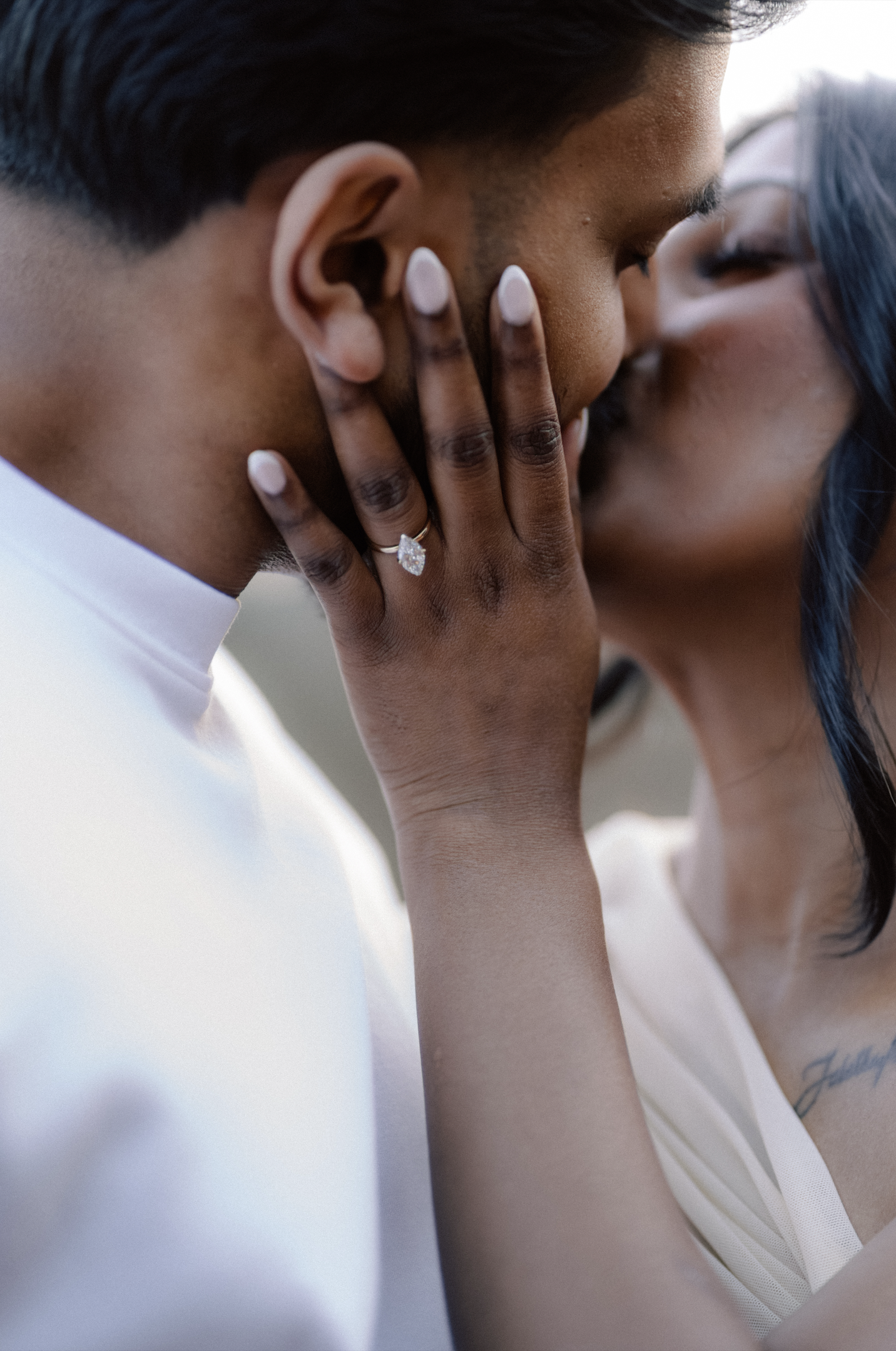 Close-up wedding portrait of a romantic couple kissing, focusing on the future bride's hand displaying an elegant engagement ring.