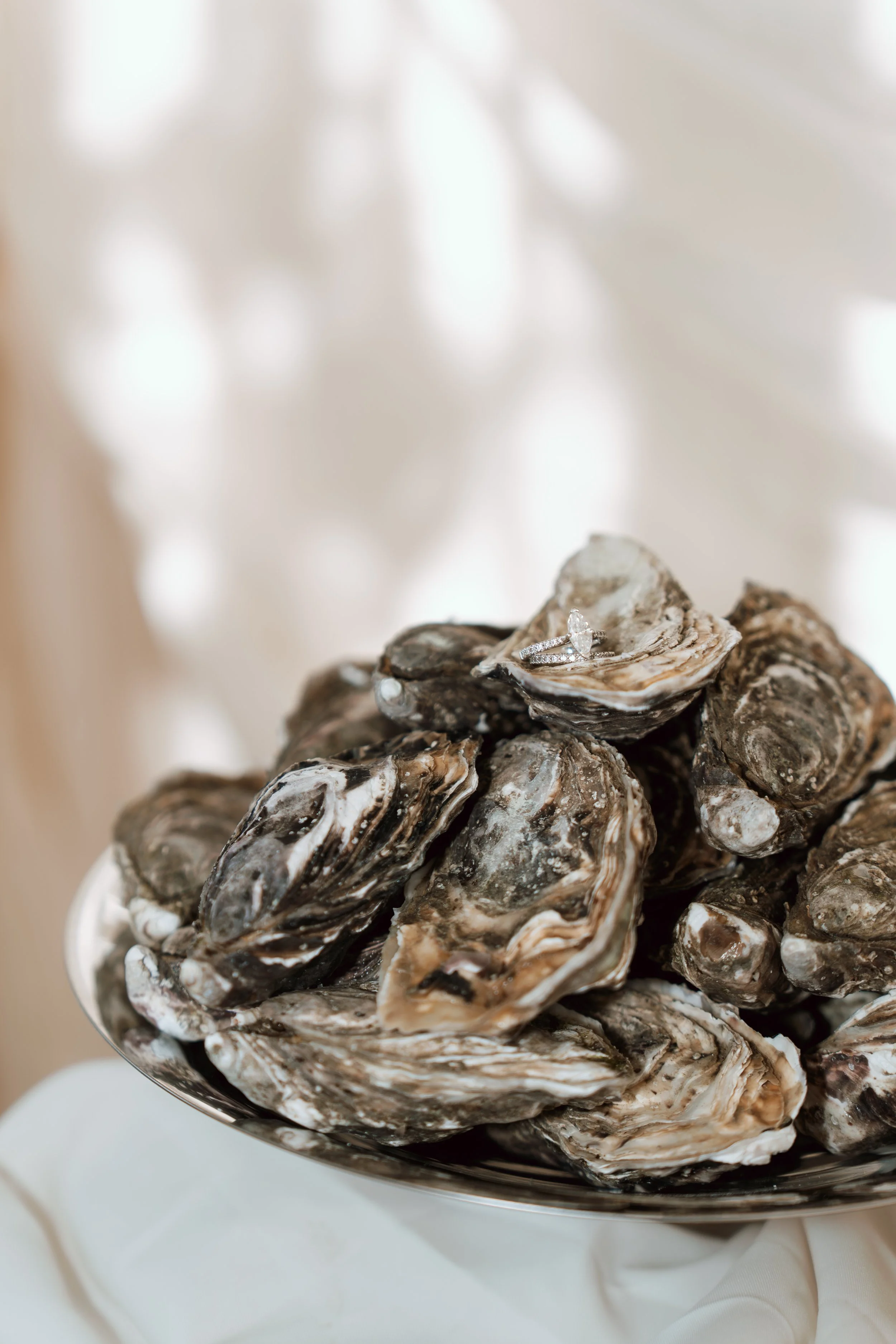 A luxury silver tray piled with fresh oysters, featuring a stunning solitaire engagement ring balanced on top for an elegant, creative proposal scene.