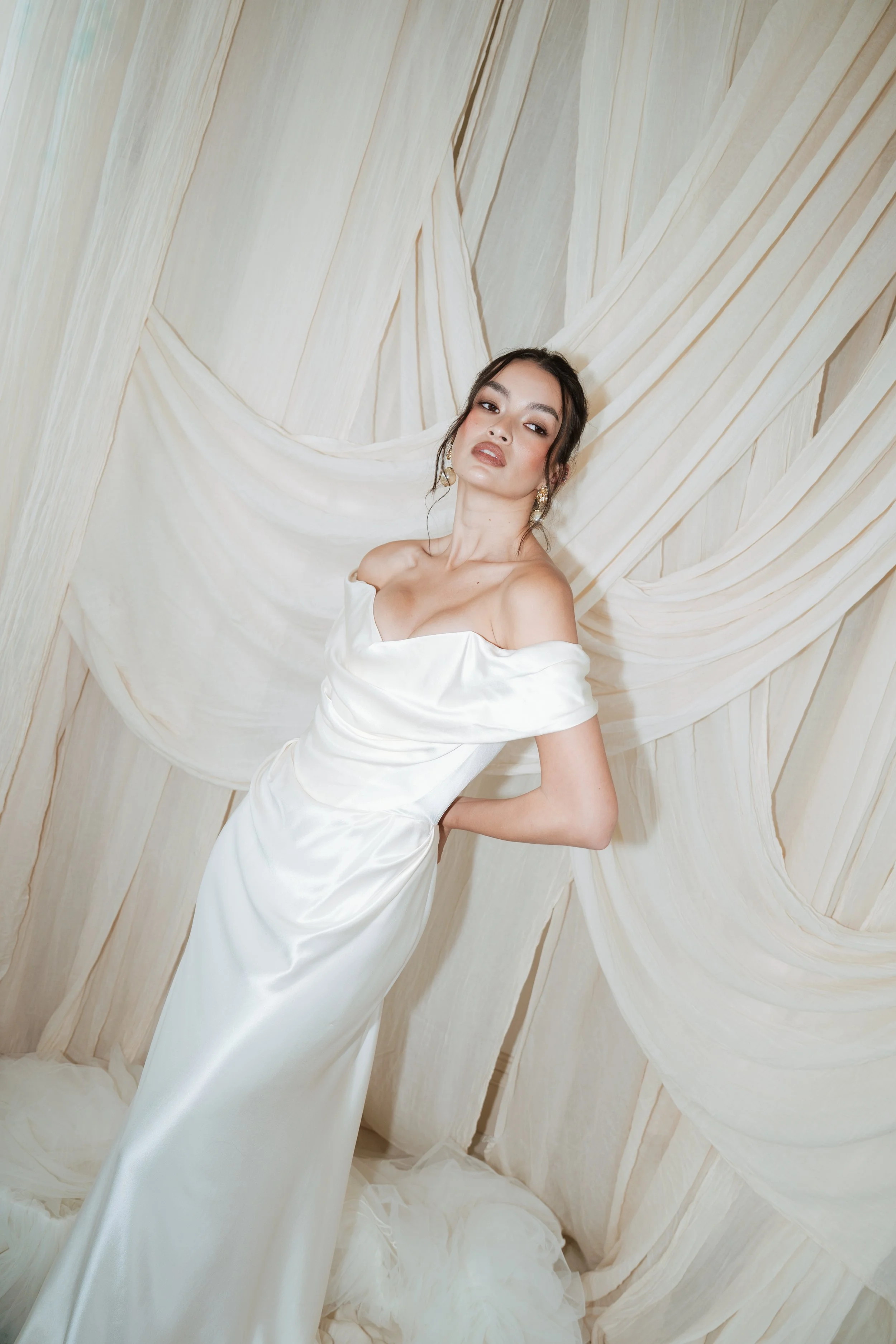 An editorial bride in a Vivienne Westwood dress posing in front of a textured beige and cream backdrop.
