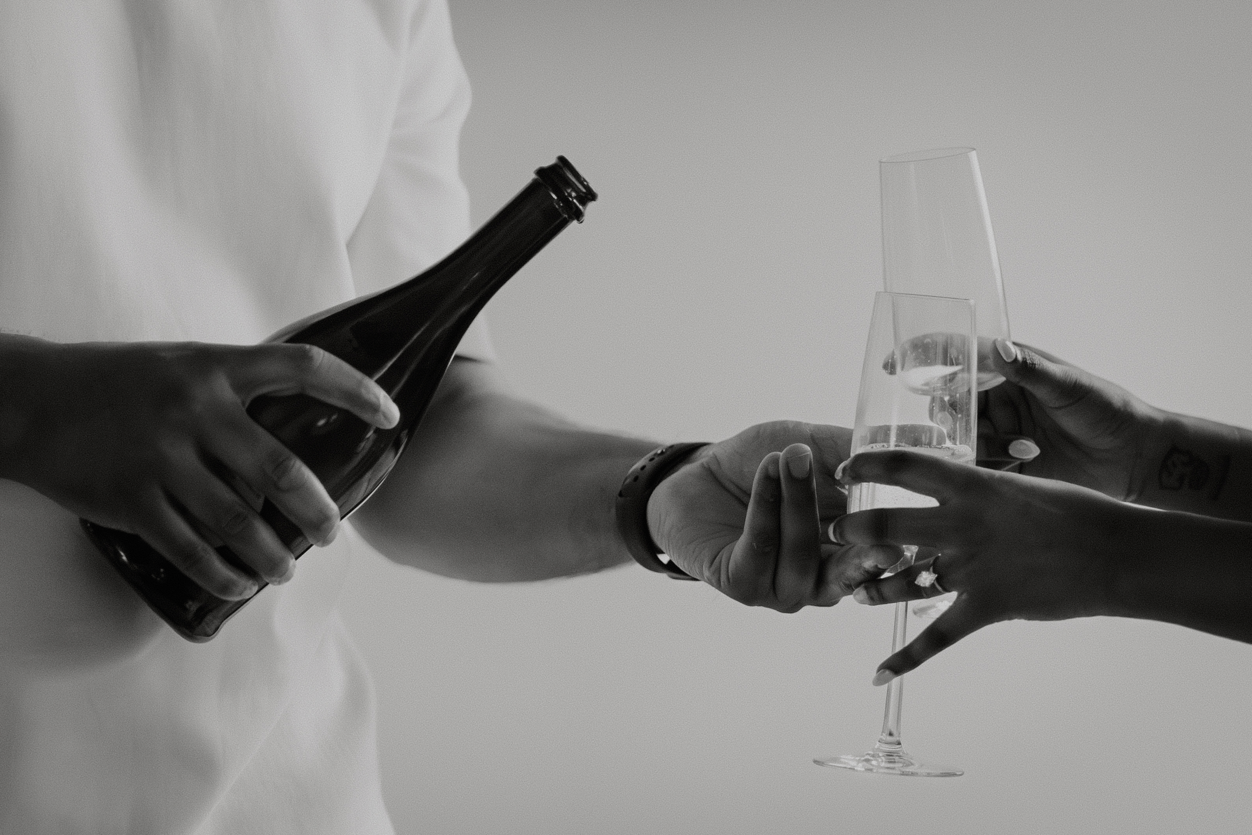 Bride and groom hands exchanging a bottle of wine and a glass of wine in a celebratory toast.