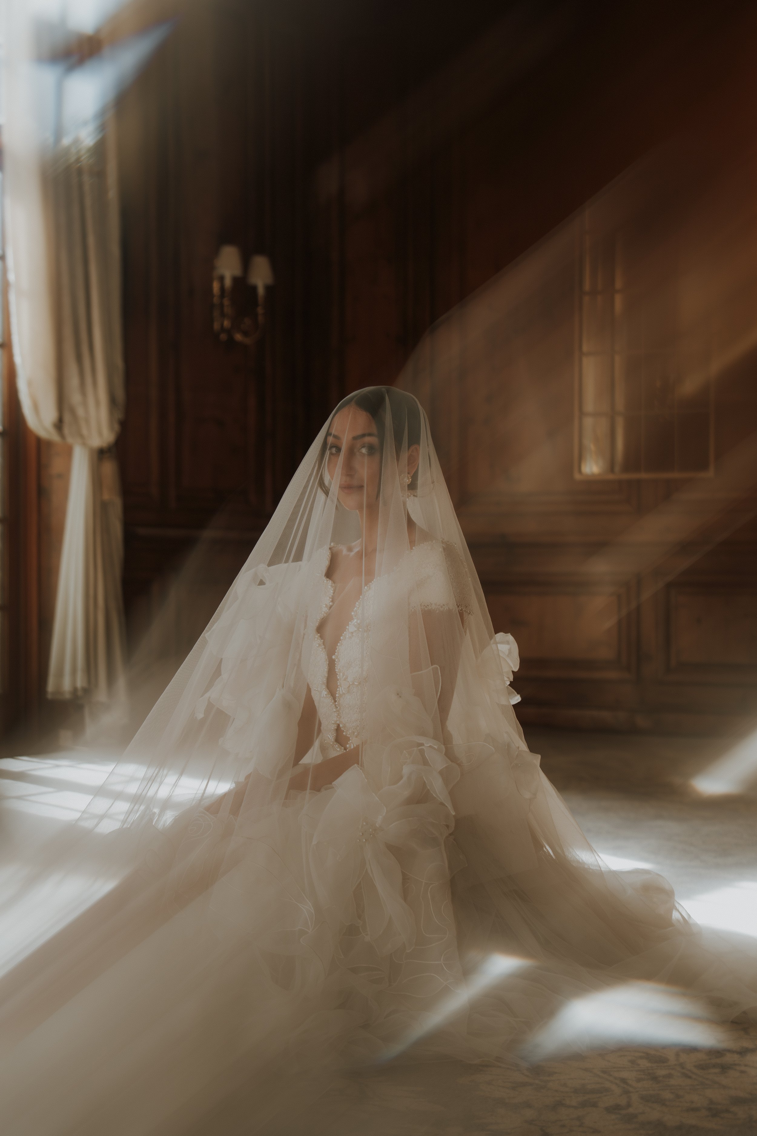 An ethereal fine art bridal portrait inside the Hedsor House ballroom, featuring a bride kneeling in warm, hazy natural light beneath a cascading wedding veil, captured by Buckinghamshire wedding photographer Jacs Batchelor.