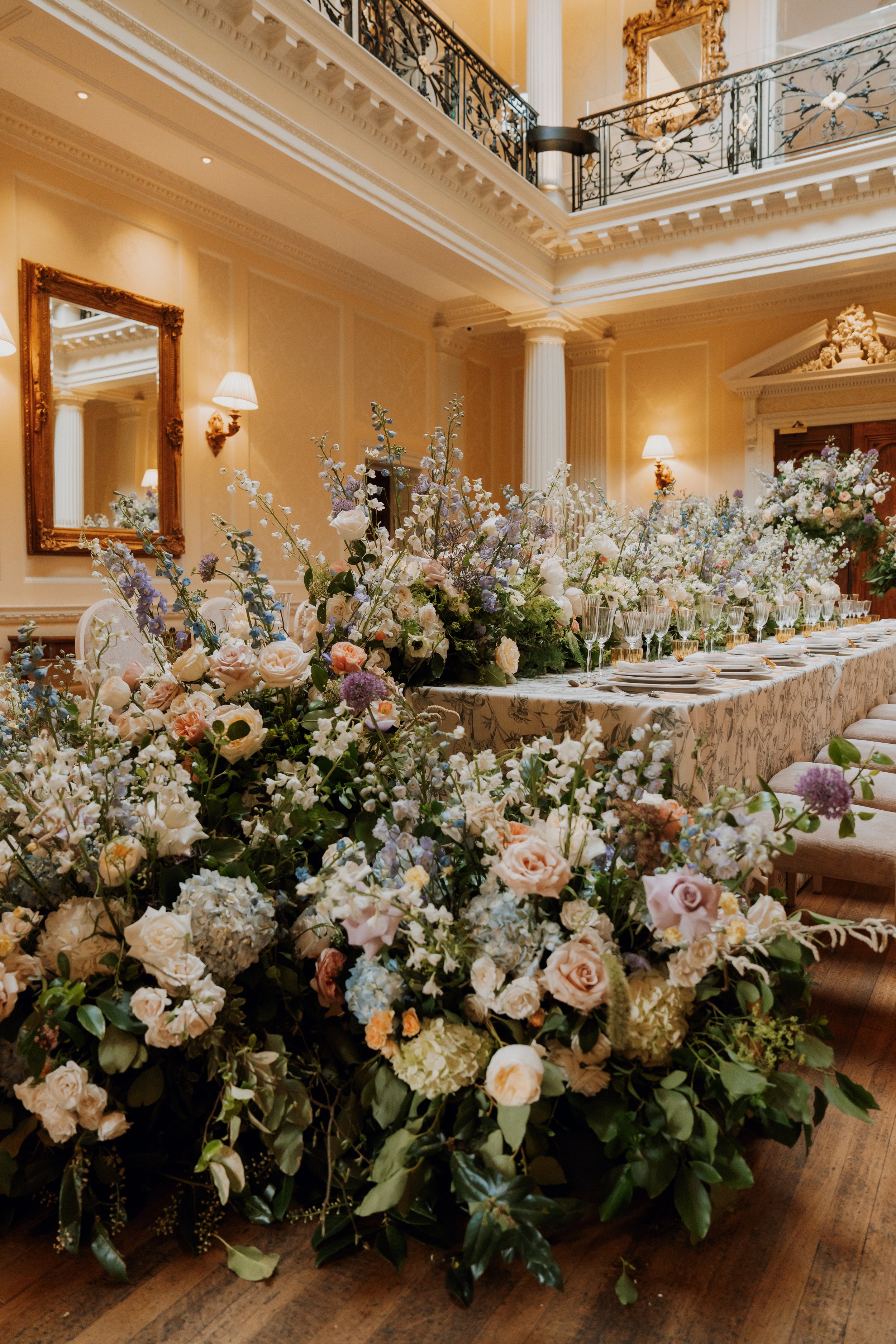 An opulent wedding reception at Hedsor House, featuring a long banquet table dressed with abundant white and pastel floral arrangements, luxury glassware, and ornate architectural details.