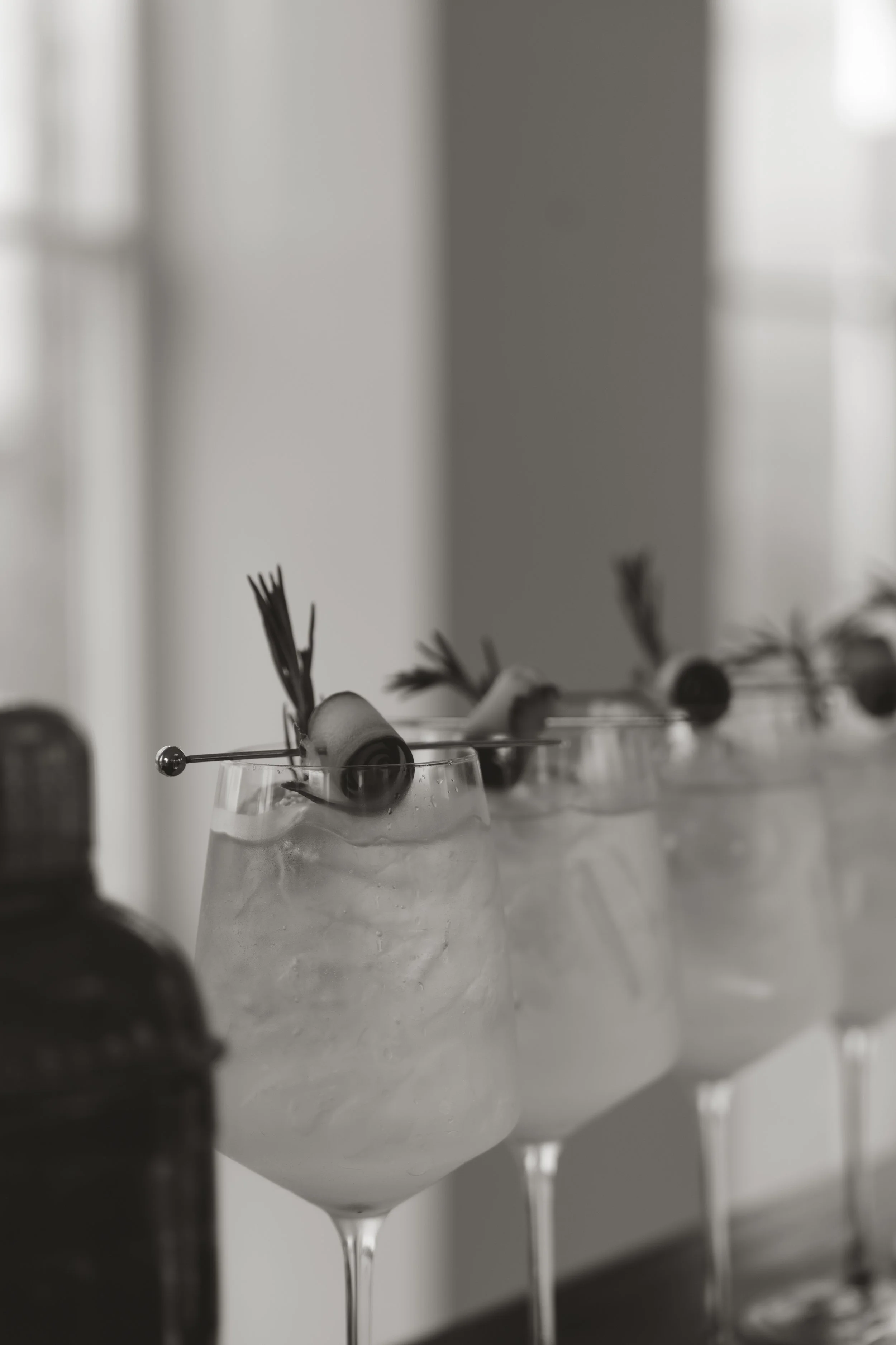 A chic, contemporary wedding bar detail shot featuring crisp, elegant martinis beautifully garnished and lined up on a sleek white surface.