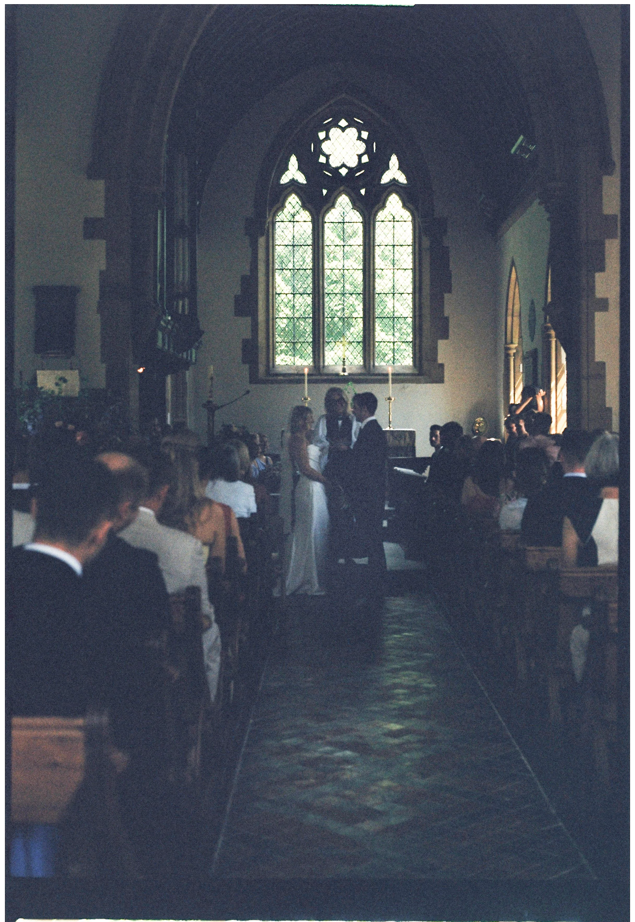 Interior of Underhill church, Sevenoaks with stained glass windows, people gathered, and a couple standing at the altar.