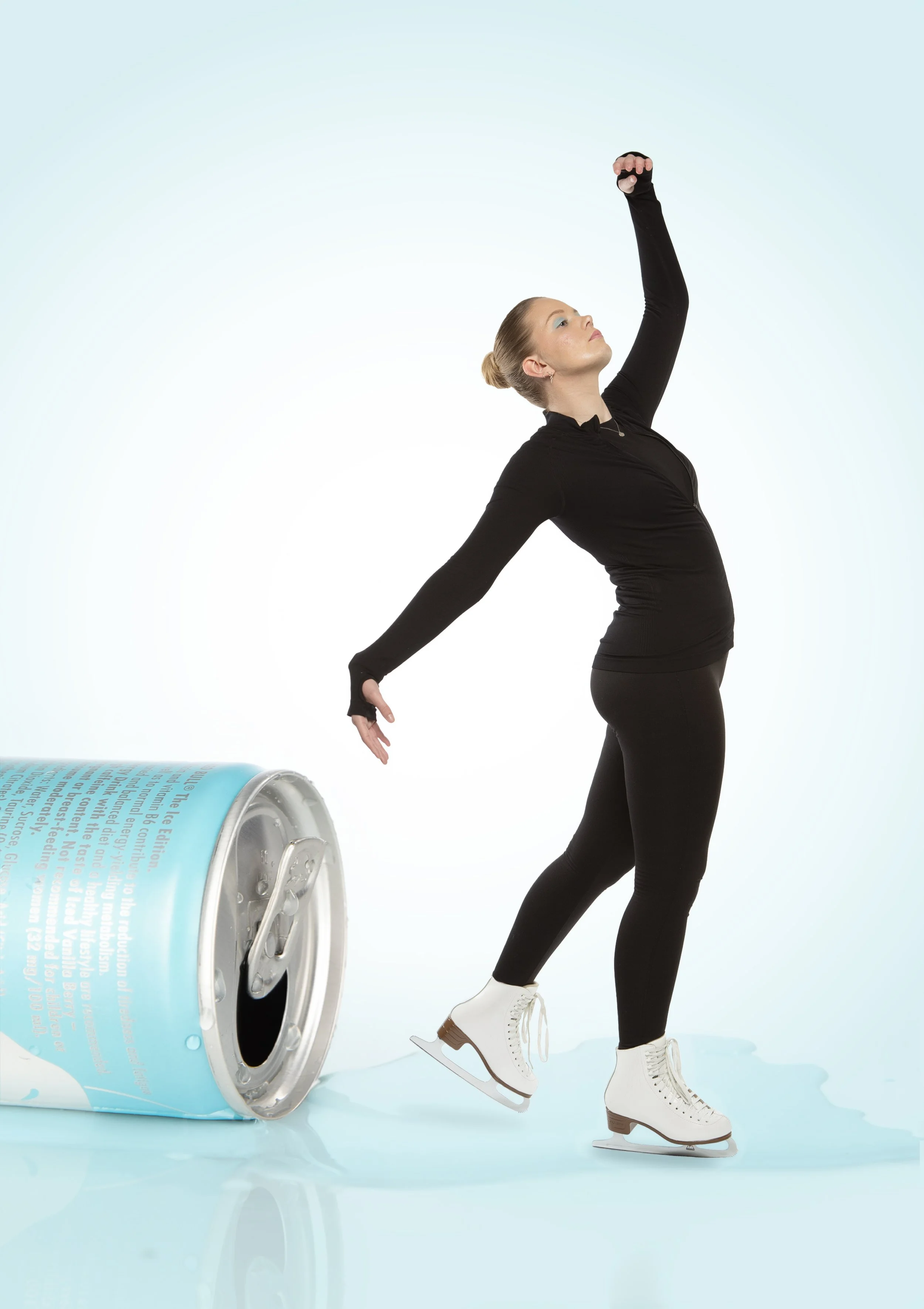 A woman in black clothing and white ice skates ice skating next to a overturned medication pill bottle.