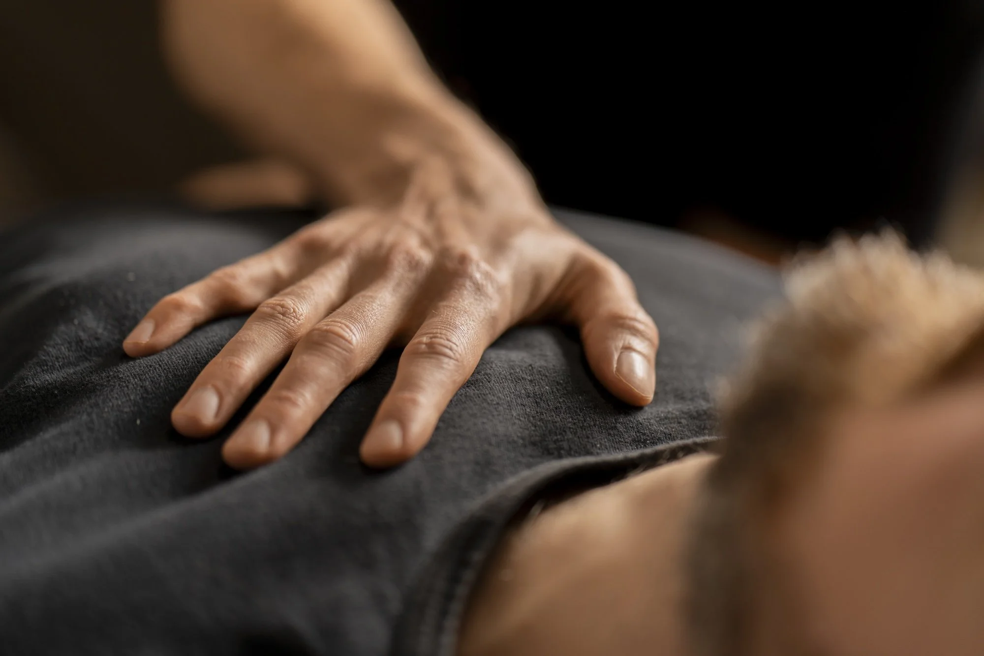 Main d'appuyant sur un autre individu, suggérant un massage ou une technique de soin, dans un contexte intime et professionnel.