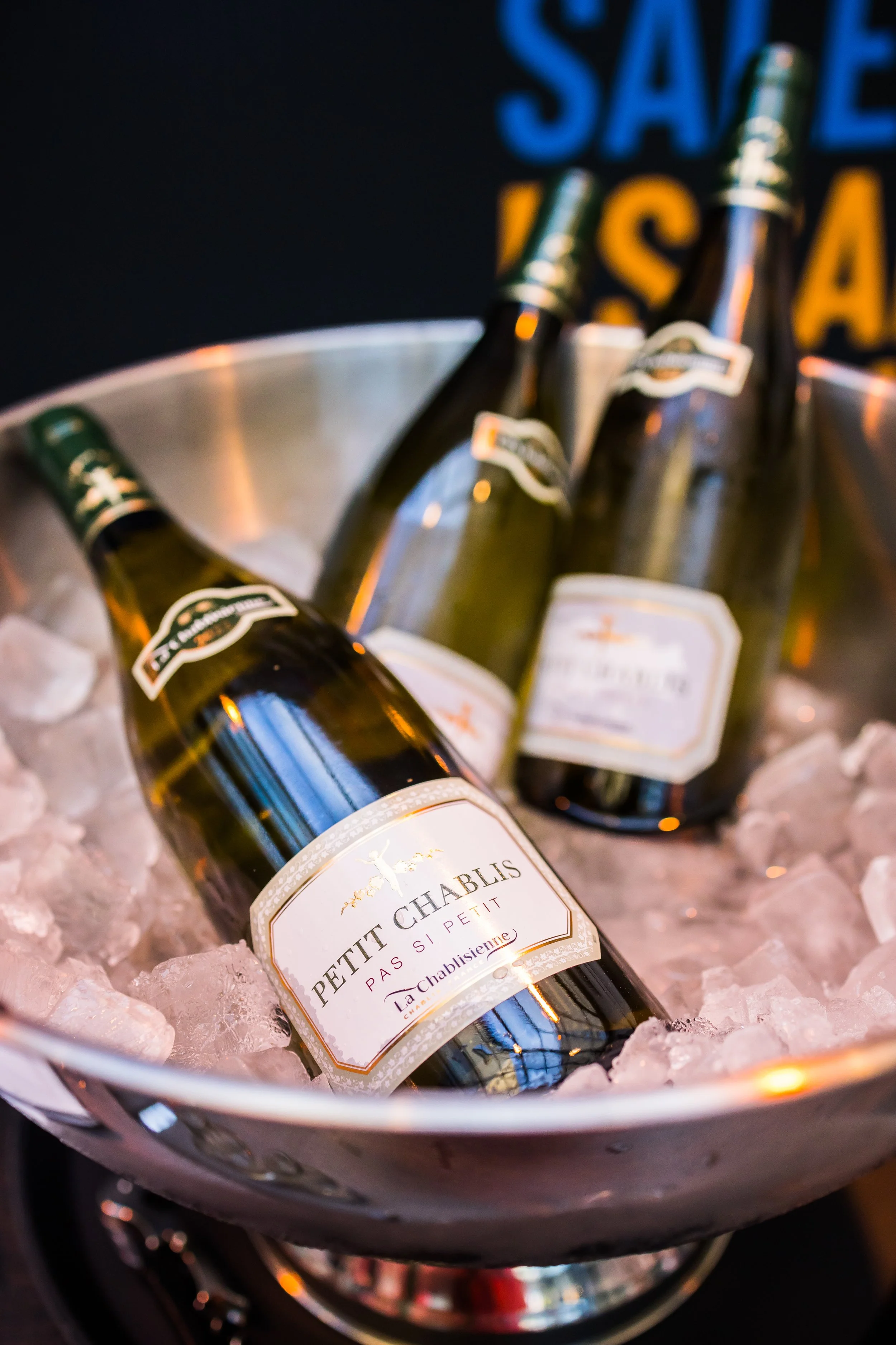 Mehrere Flaschen Petit Chablis Wein liegen in einem Eiskübel, der mit Eis gefüllt ist.