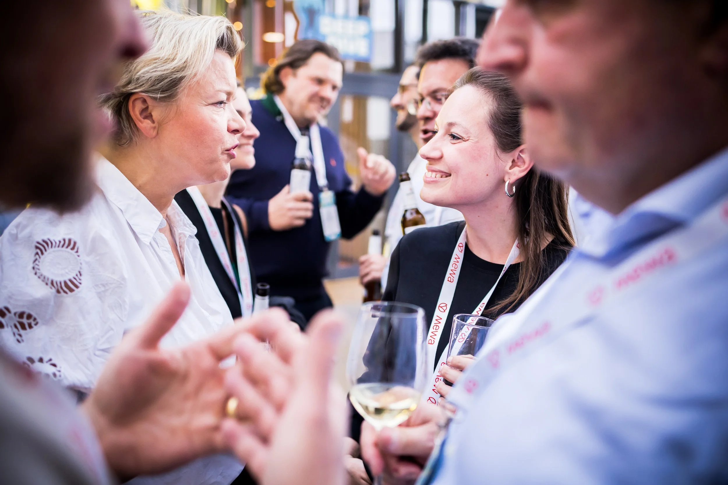 Menschen beim Gespräch auf einer Party, einige halten Getränke, lachen und unterhalten sich in einer festlichen Atmosphäre.