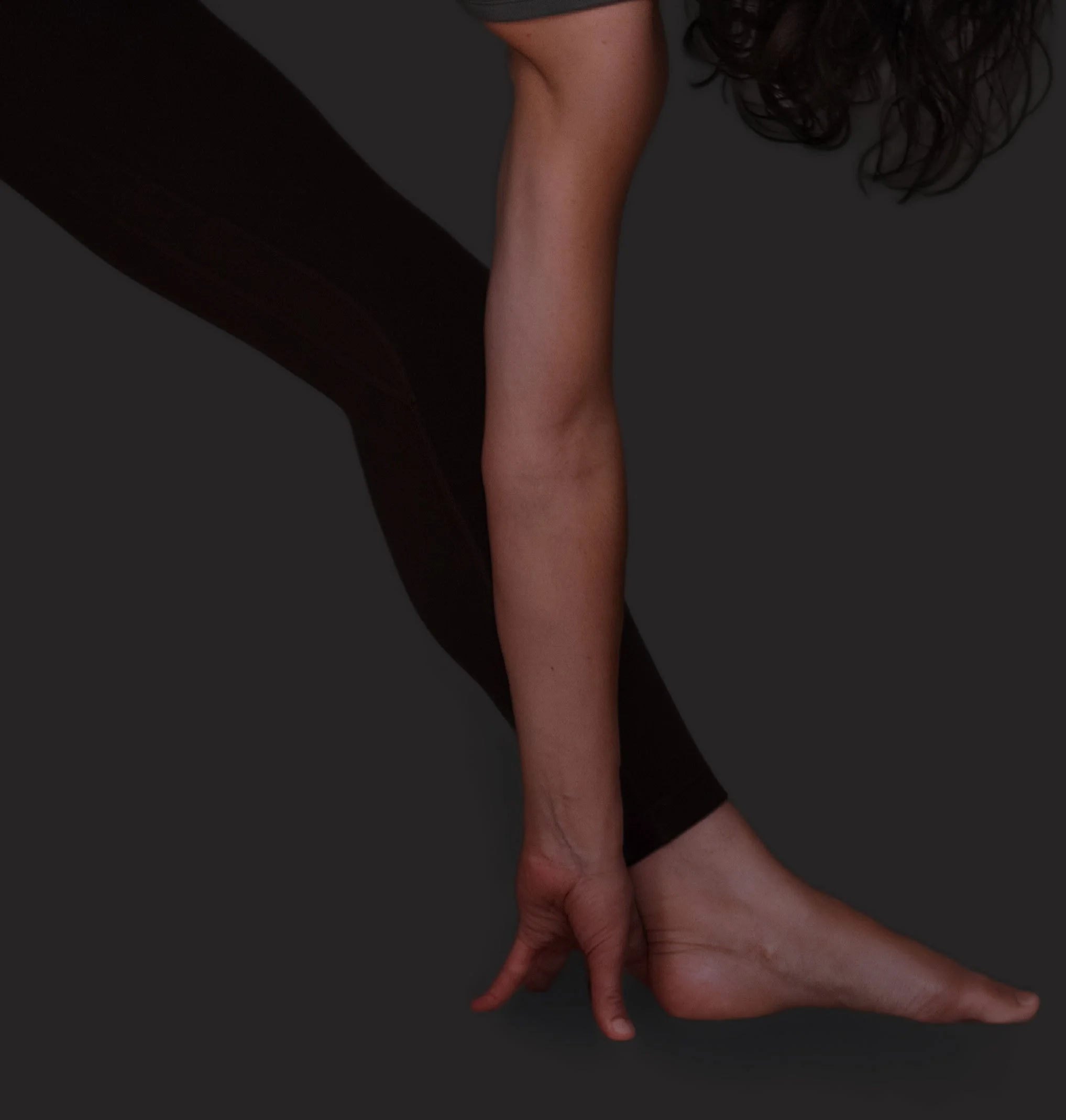A close-up of a person's hand and forearm, with the person kneeling or crouching on a dark surface. The person's hand is resting on their knee, and their dark, curly hair is partially visible in the background.
