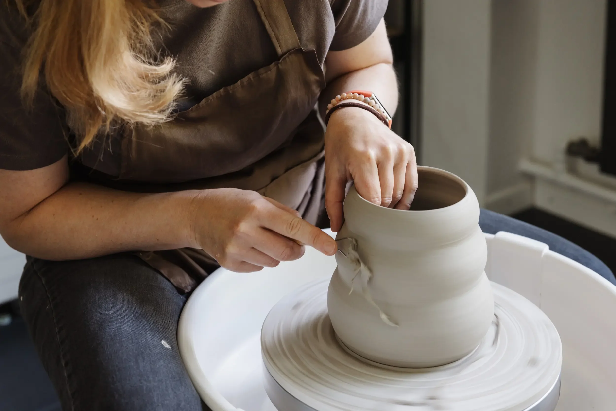 Eine Person formt mit der Hand aus Ton eine Vase auf einer Drehmaschine.