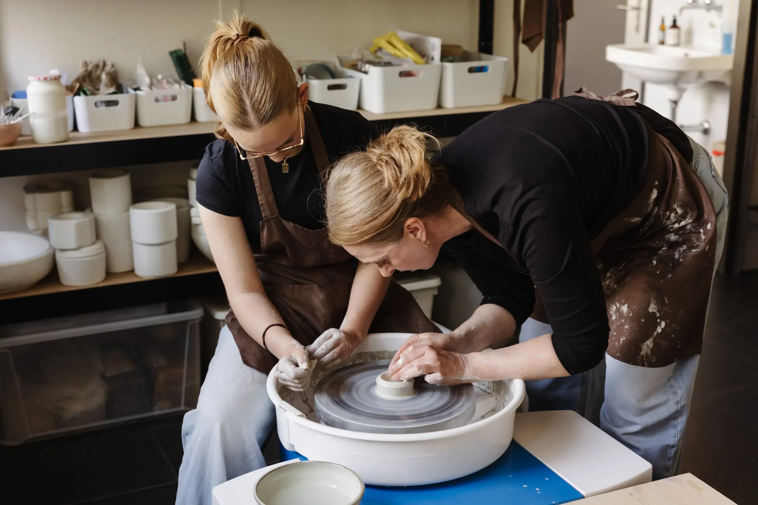 Zwei Frauen arbeiten zusammen an einem keramischen Töpferprojekt an einer Drehscheibe in einer Werkstatt.