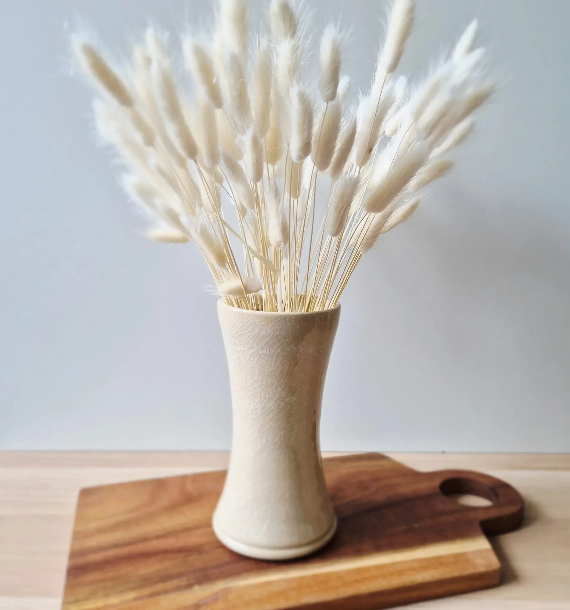 Weiße getrocknete Grase und Blumen in einer Vase auf einem Holztablett