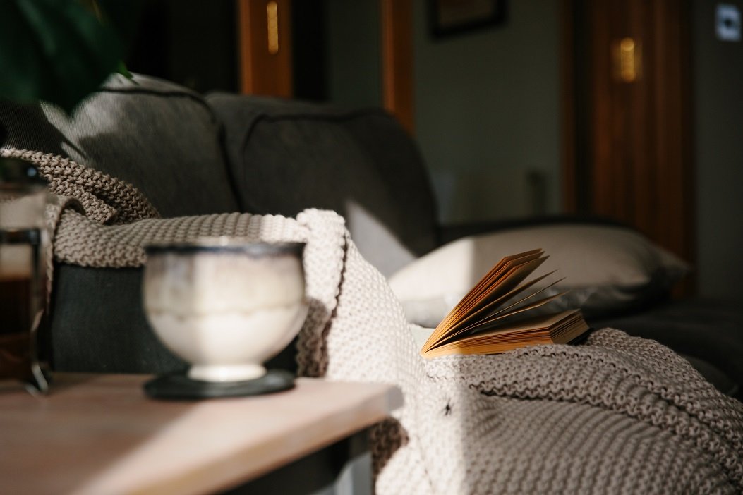  Livre ouvert posé sur un tricot beige, éclairé par une lumière douce près d’une tasse en céramique.