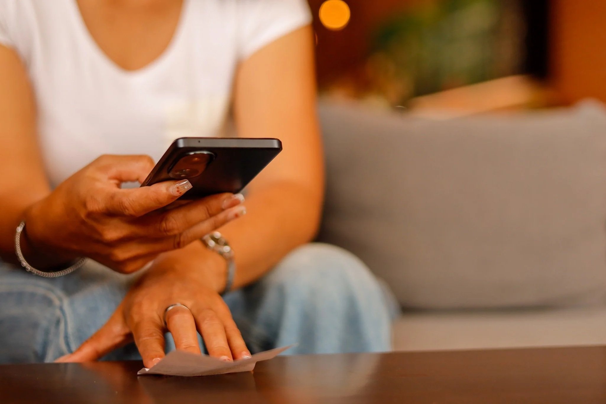 Personne assise sur un canapé, entrant une adresse web sur son téléphone, lumière chaude d’intérieur.