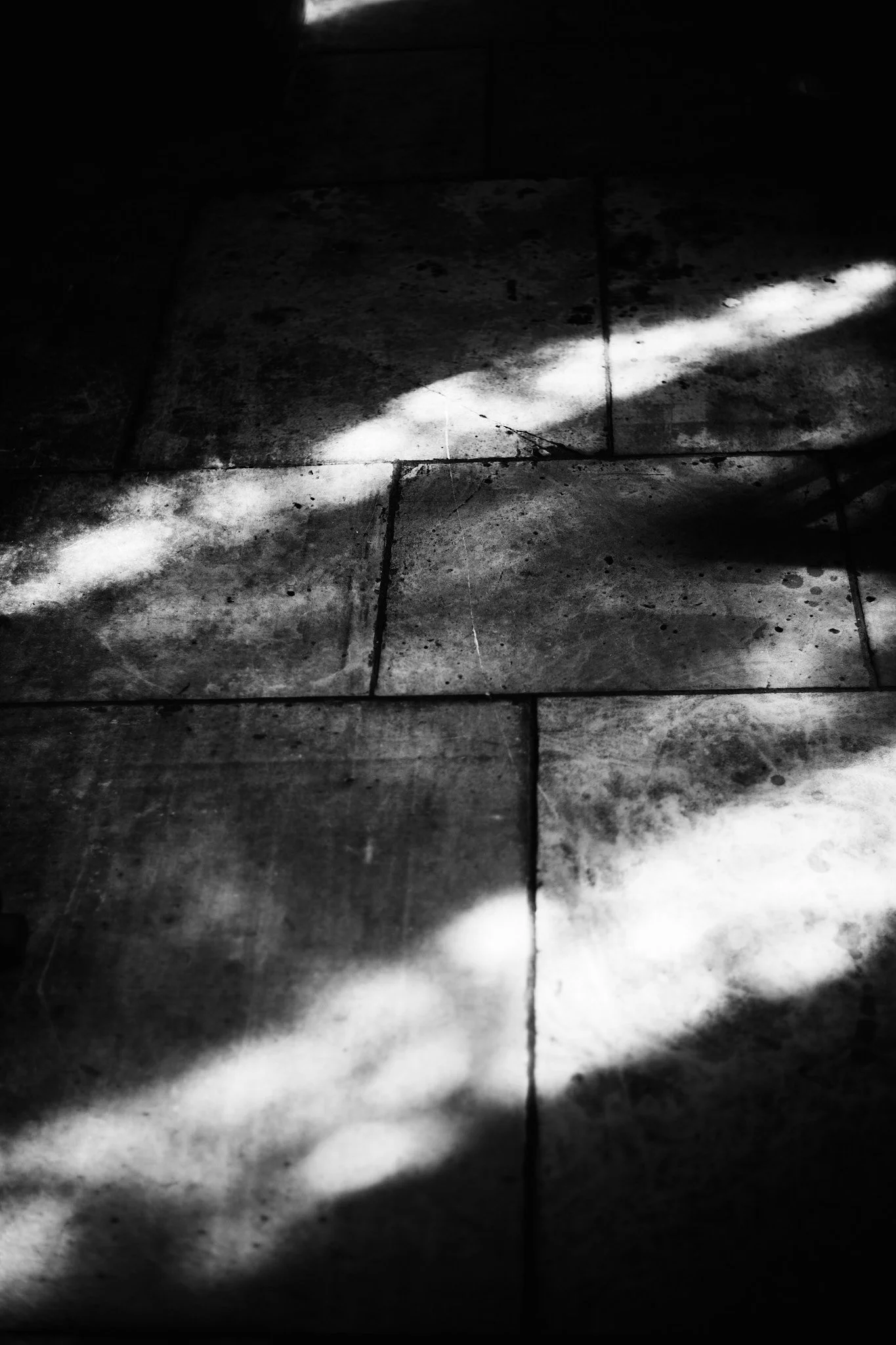 Black-and-white photo of a tiled floor with light and shadow streaks crossing certain tiles.