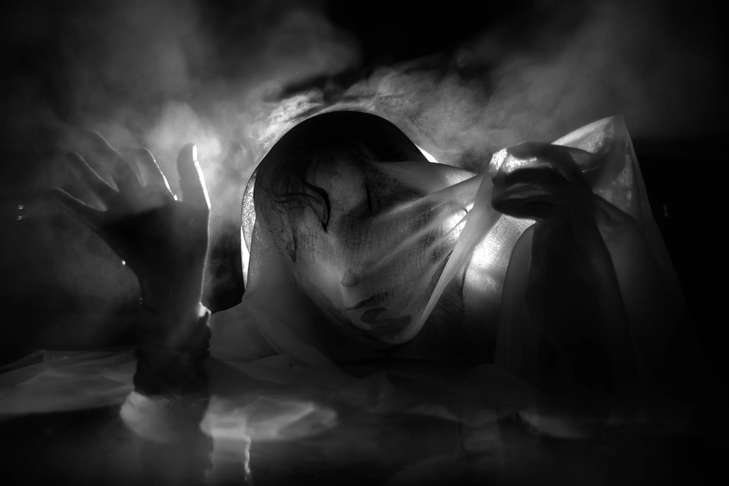 Black and white photograph of a person partially obscured by reflections and translucent material, creating an abstract layered portrait.