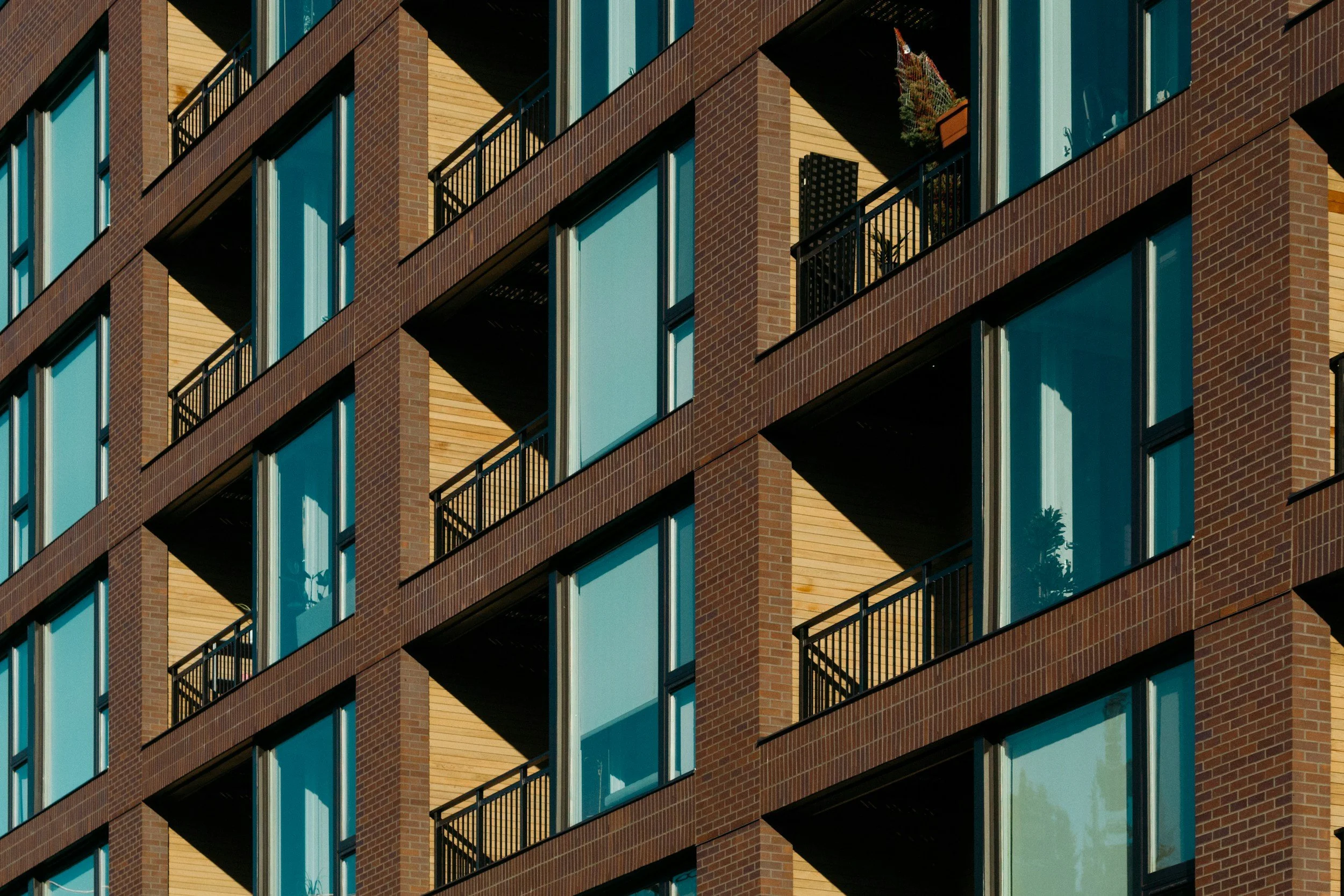 Close-up of a modern multi-story apartment building with brick exterior, glass windows, and small balconies with black railings.