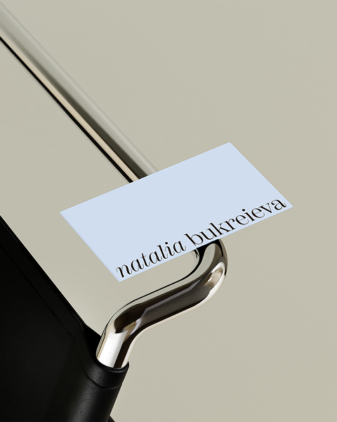 Close-up of a light-colored desk with a black edge, a metal rail, and a small white card with the name 'Natalia Bukreieva' written on it.