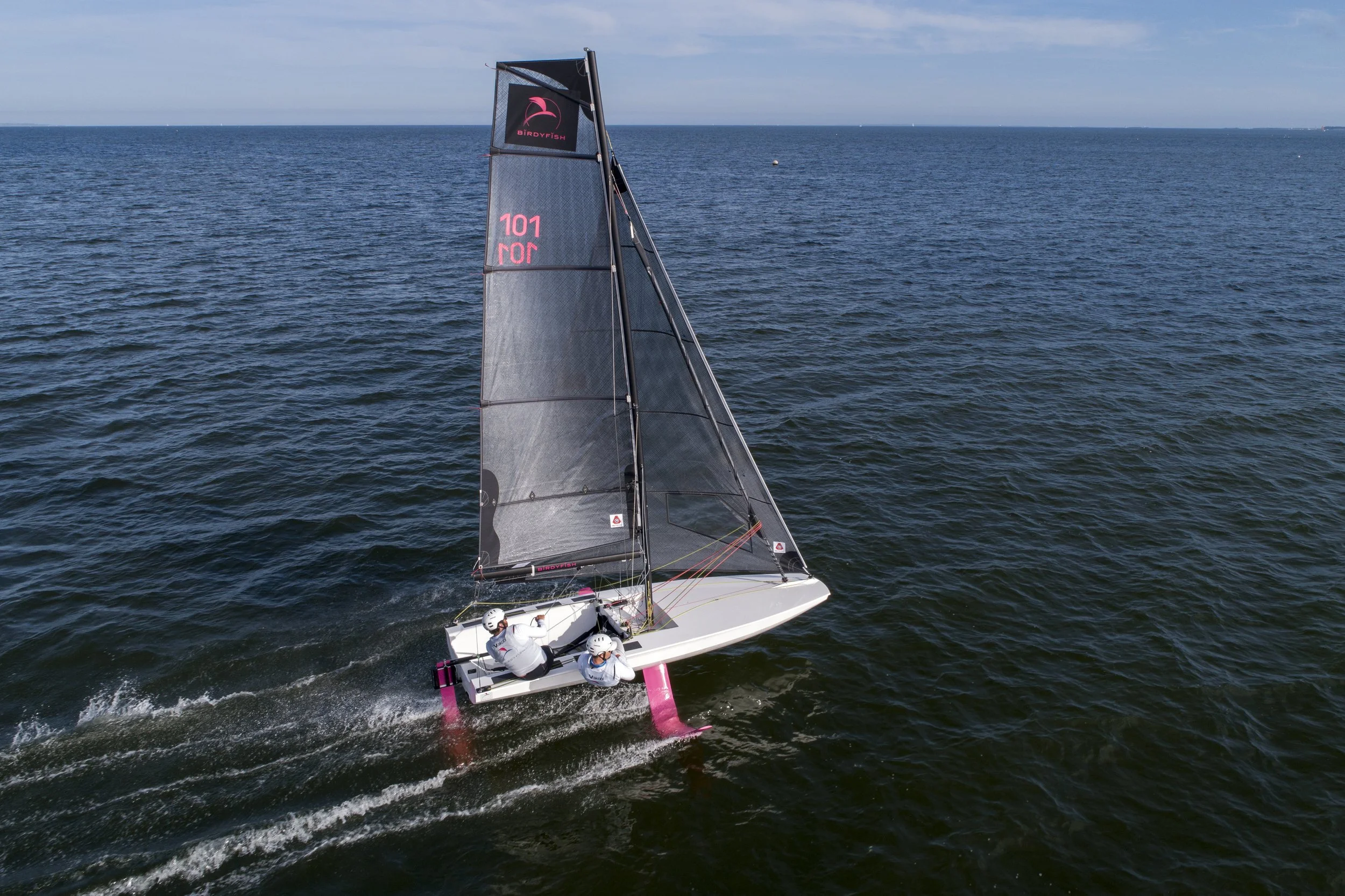 A sailboat with pink and black sails racing across the ocean on a clear day.