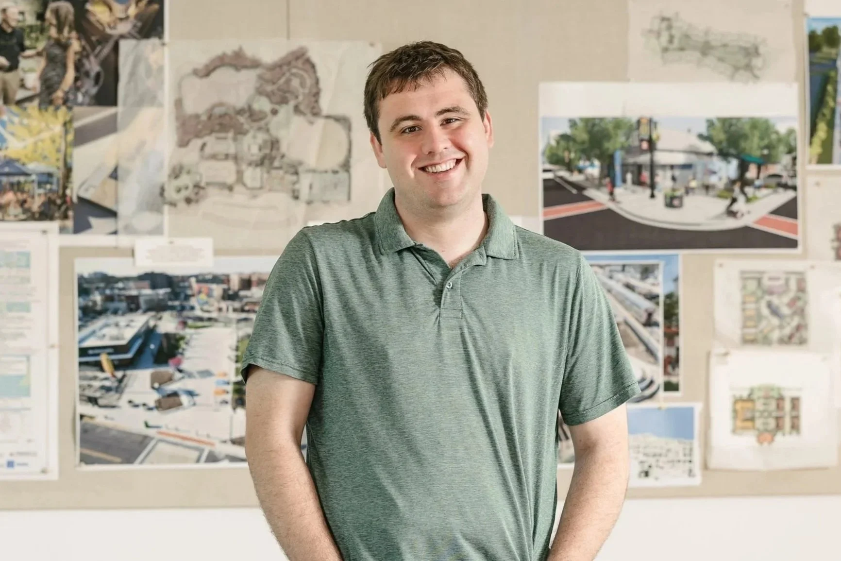 Andrew Dunham wearing a green polo shirt, standing in front of a wall with various architectural and city planning drawings and photographs.