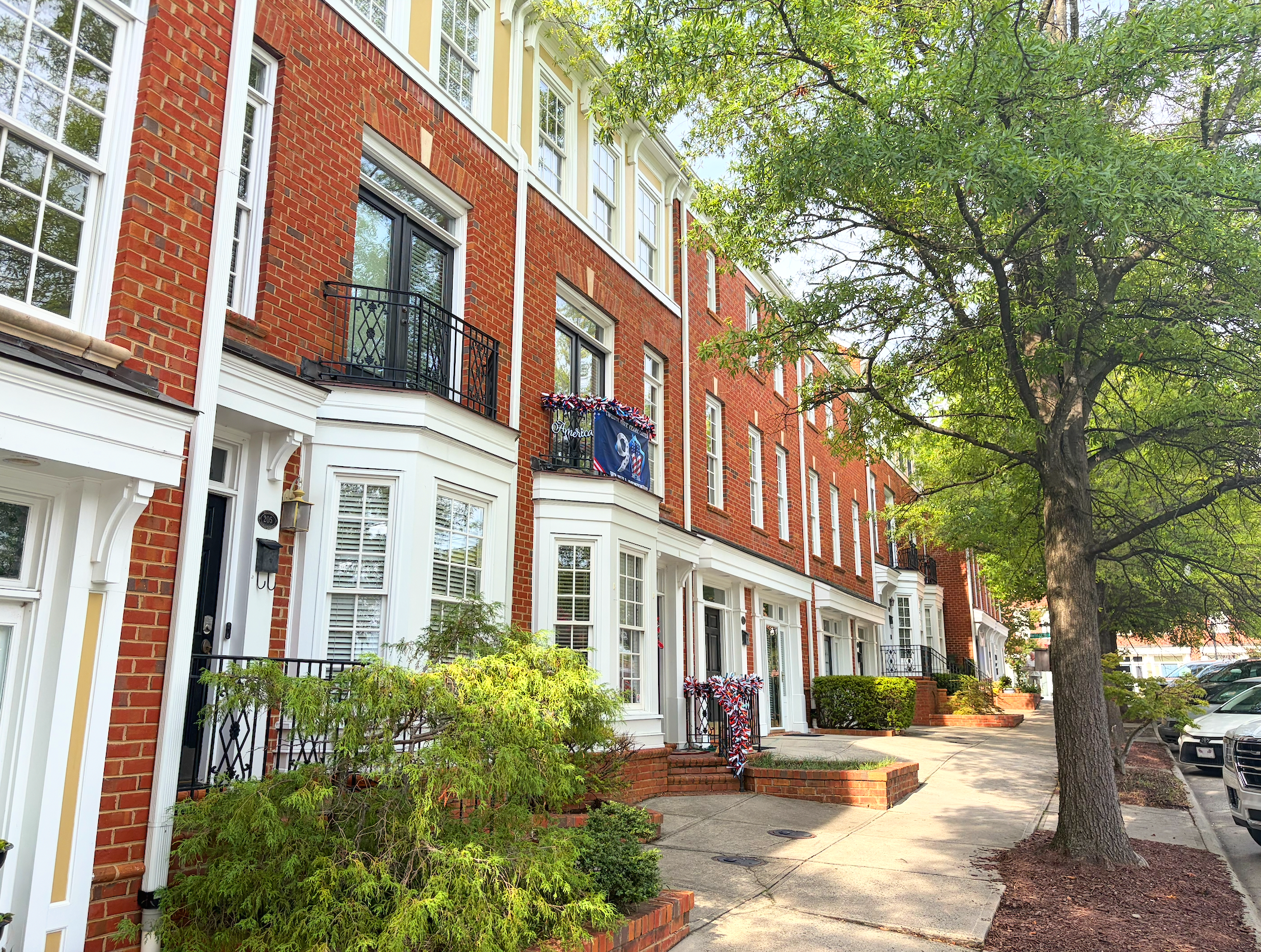 Red brick residential buildings with white trim, black iron balconies, and a tree-lined sidewalk.