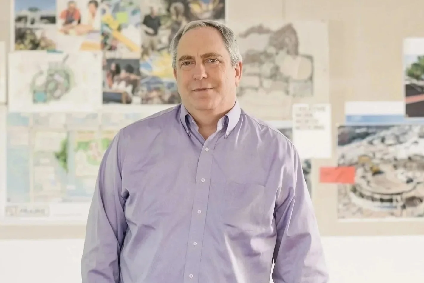 Michael Blue standing in front of a wall with various architectural and construction plans and maps.