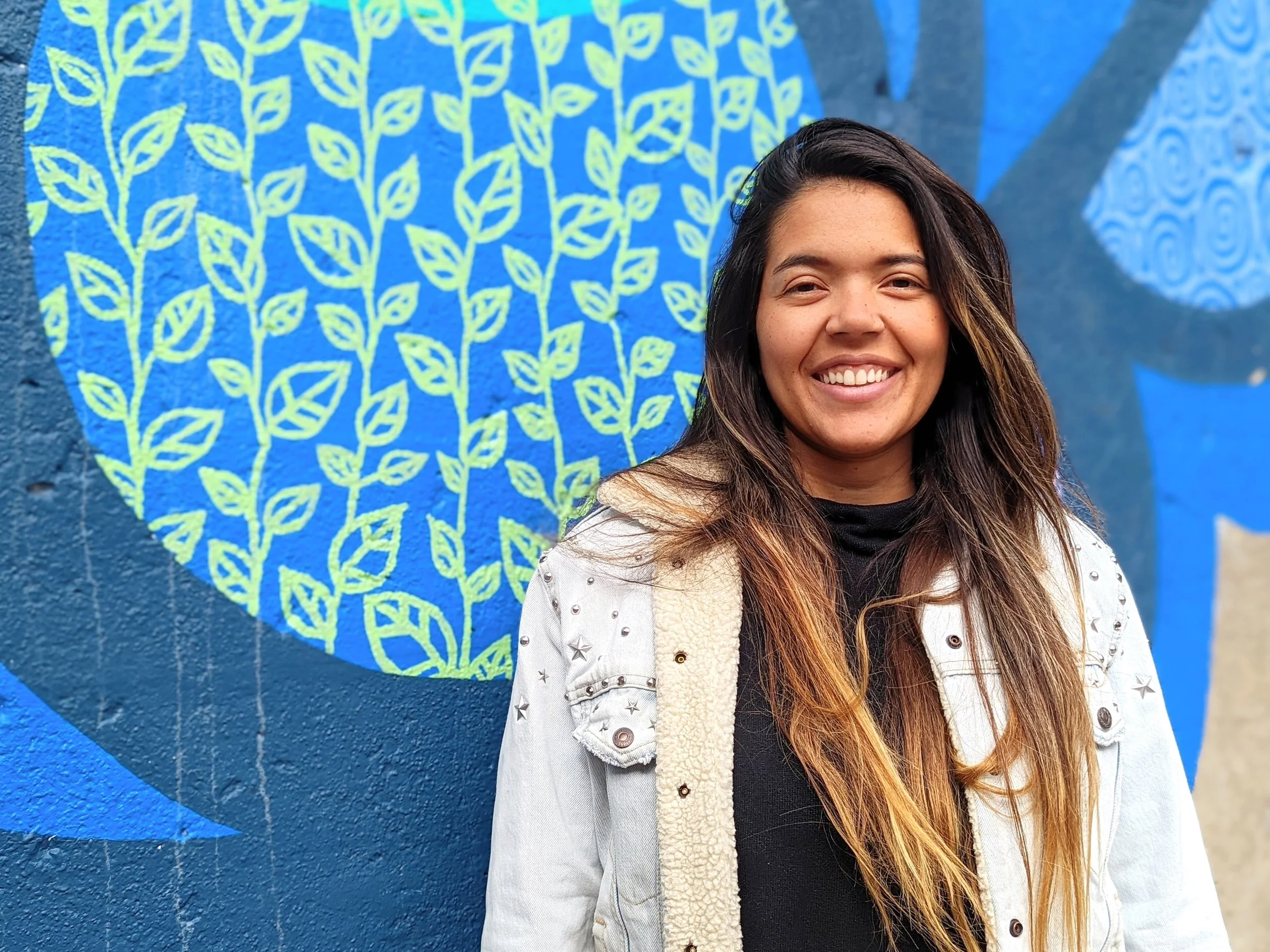 Greta Diaz standing in front of a blue wall with yellow leaf patterns and a blue mural with swirl designs.
