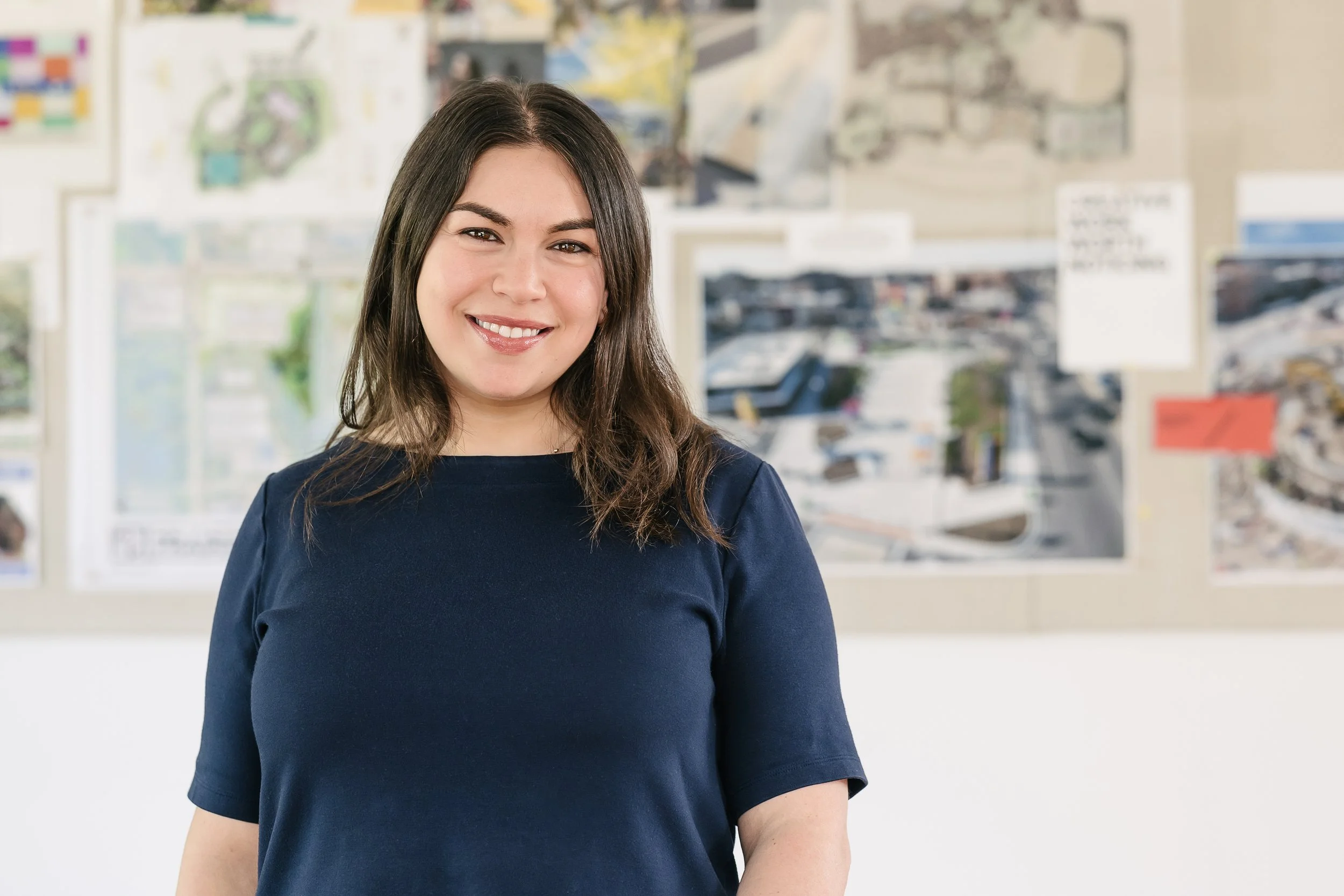 Francie Lawrence smiling in an office or classroom with maps and notices on the wall behind her.