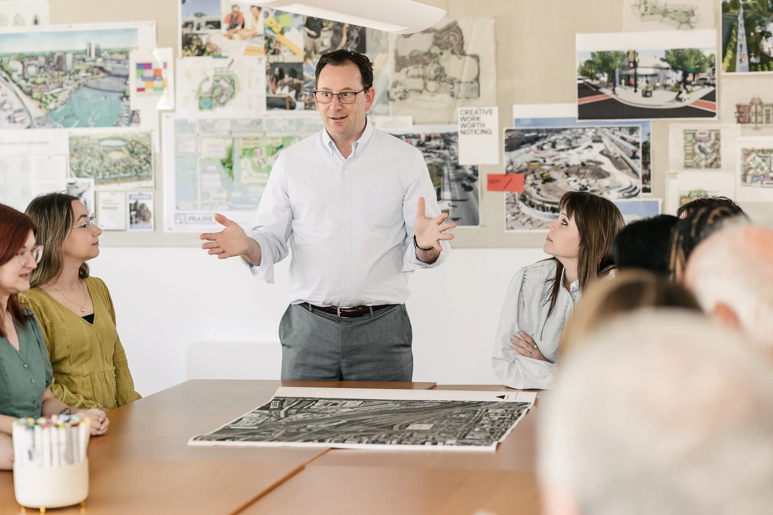 Scott Goldstein giving a presentation to a group of women in a meeting room decorated with architectural plans and images on the wall.
