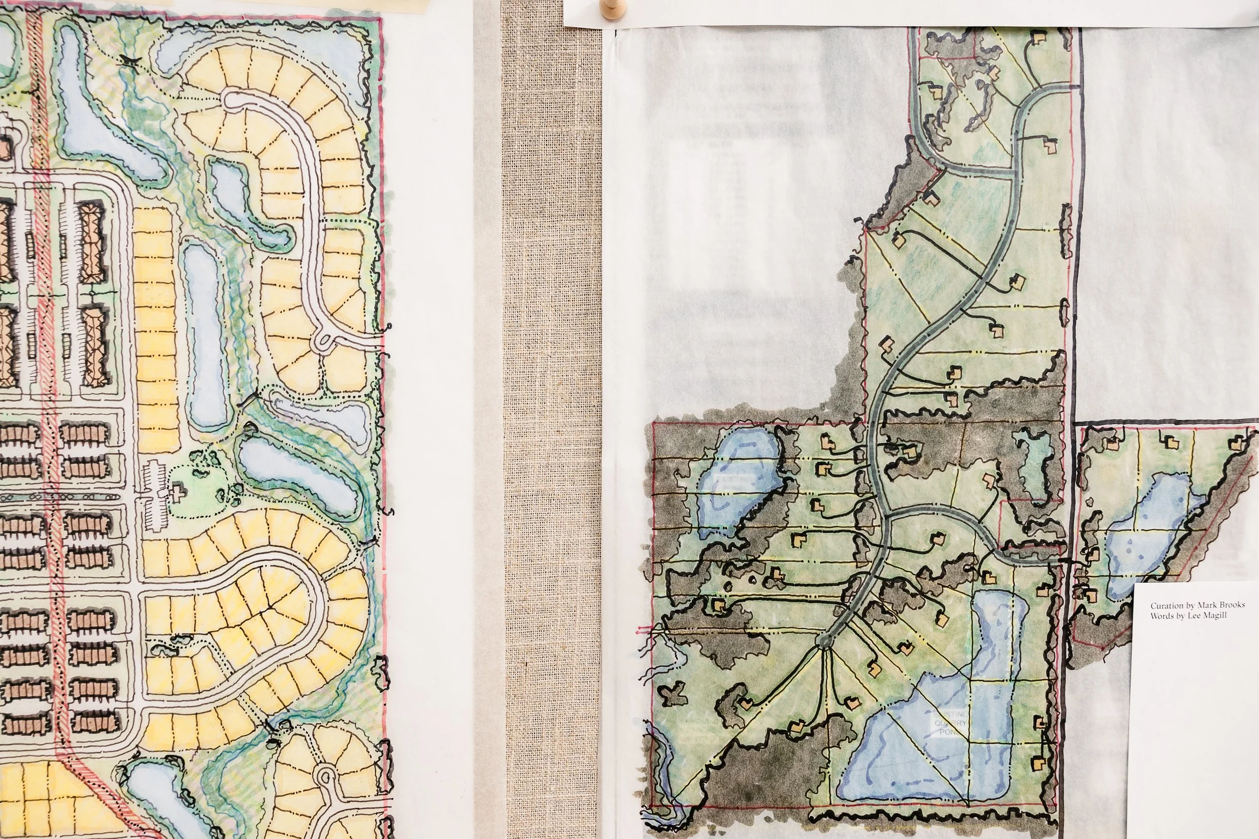 Aerial view of two detailed landscape architectural plans with water features, winding roads, and residential areas, displayed on fabric surfaces.