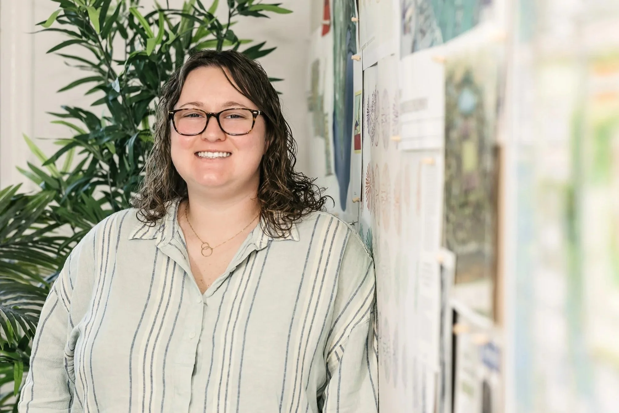 Alisa Courey smiling in front of a wall with posters and a large green plant.