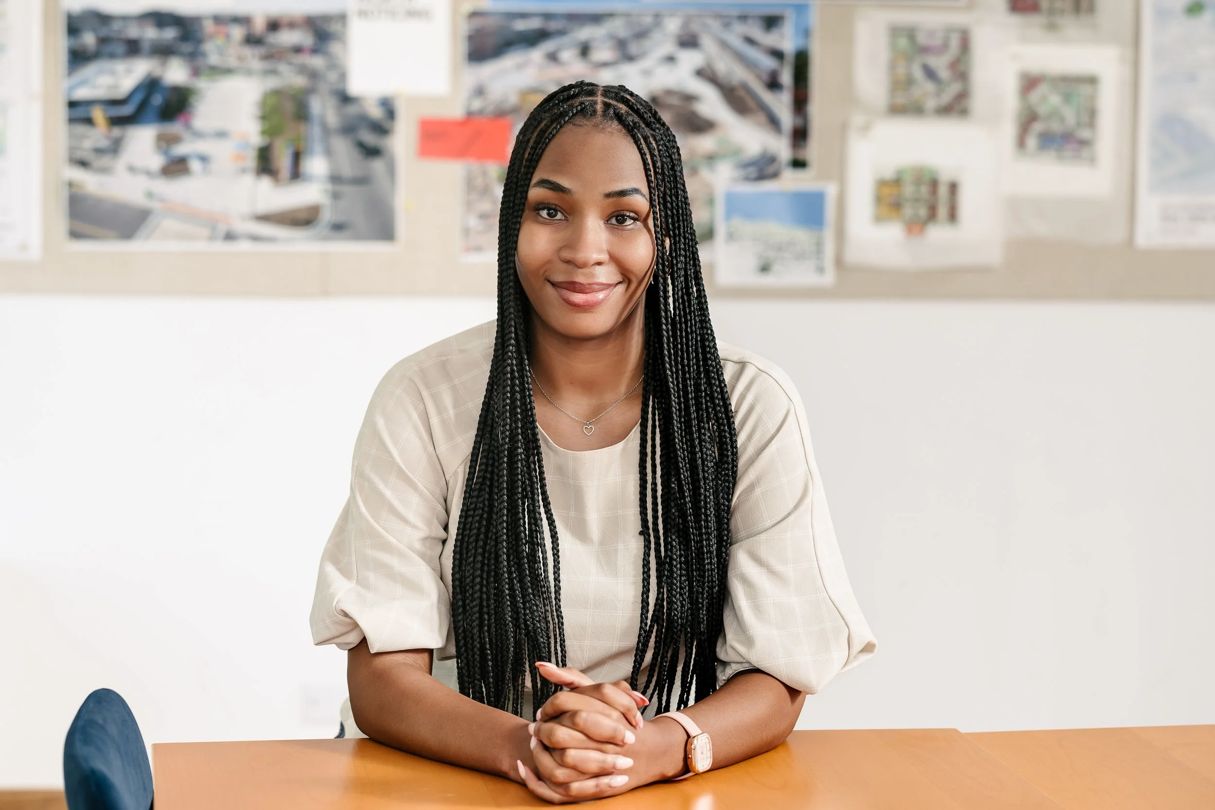 Kameria Nichols-Hazziez sitting at a table in a room with a bulletin board in the background. She is smiling and has her hands folded on the table.